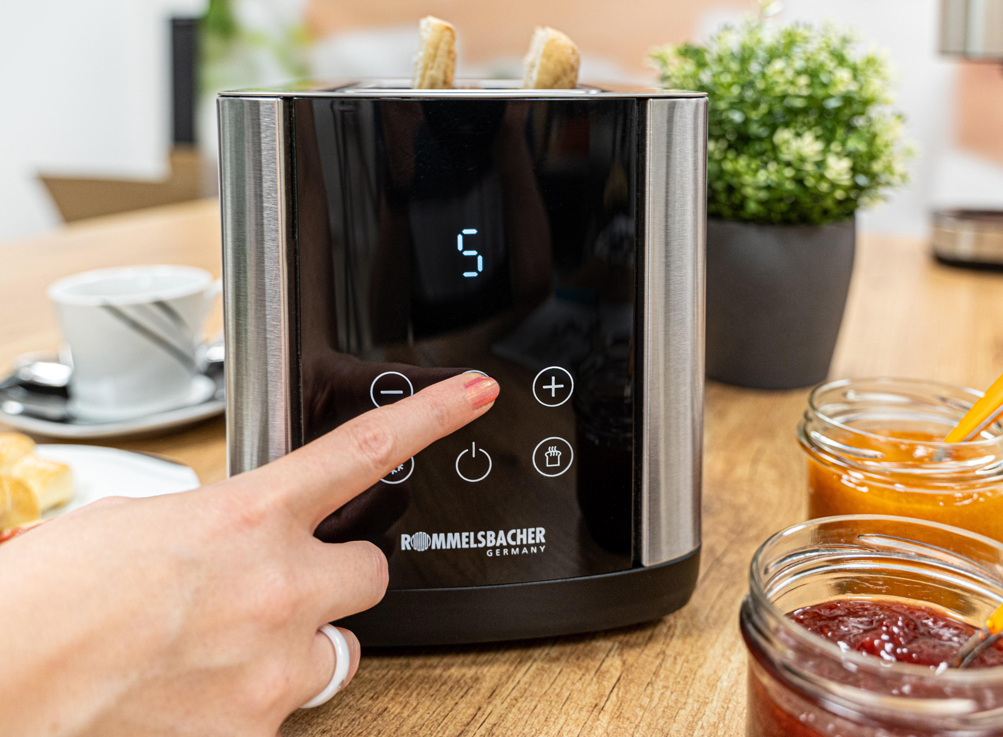 Toaster mit Brot, ein Finger drückt einen Knopf, und Gläser.