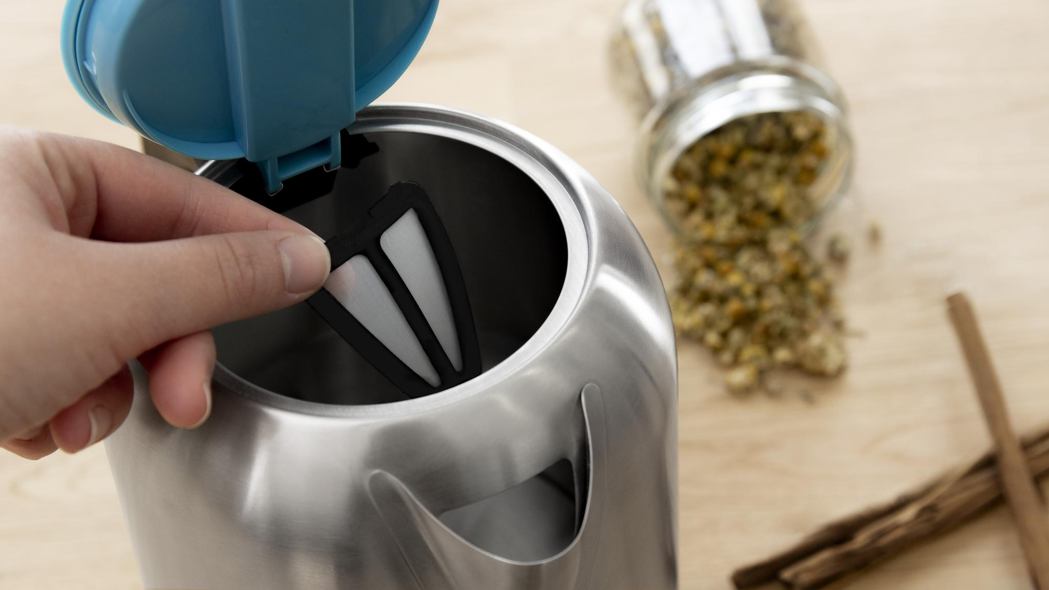 Persona insertando un filtro en una tetera eléctrica de acero inoxidable. Té de manzanilla en el fondo.