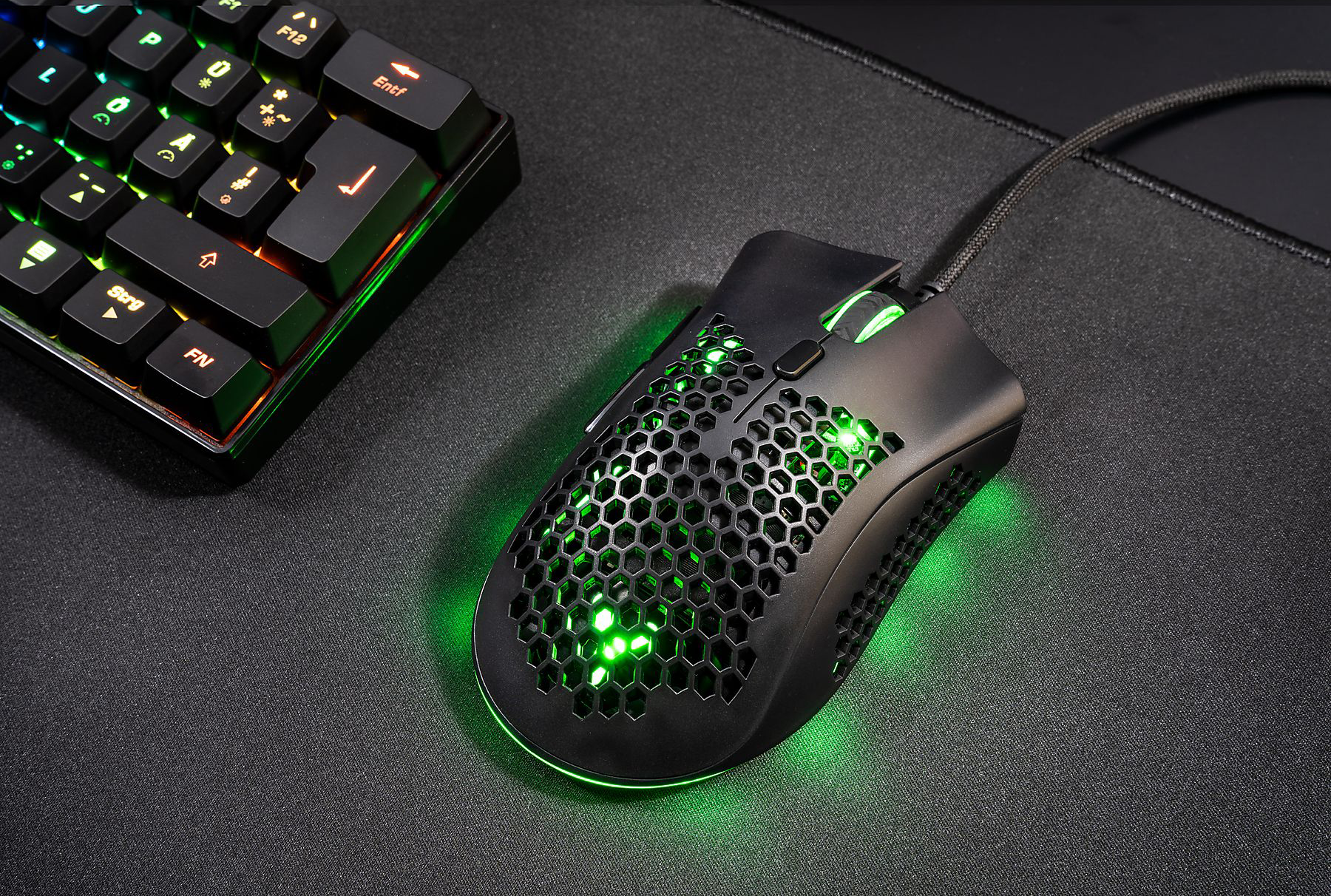 Fekete gamer egér egy egérpadon, billentyűzet a háttérben. Az egér méhsejt-mintázatú.