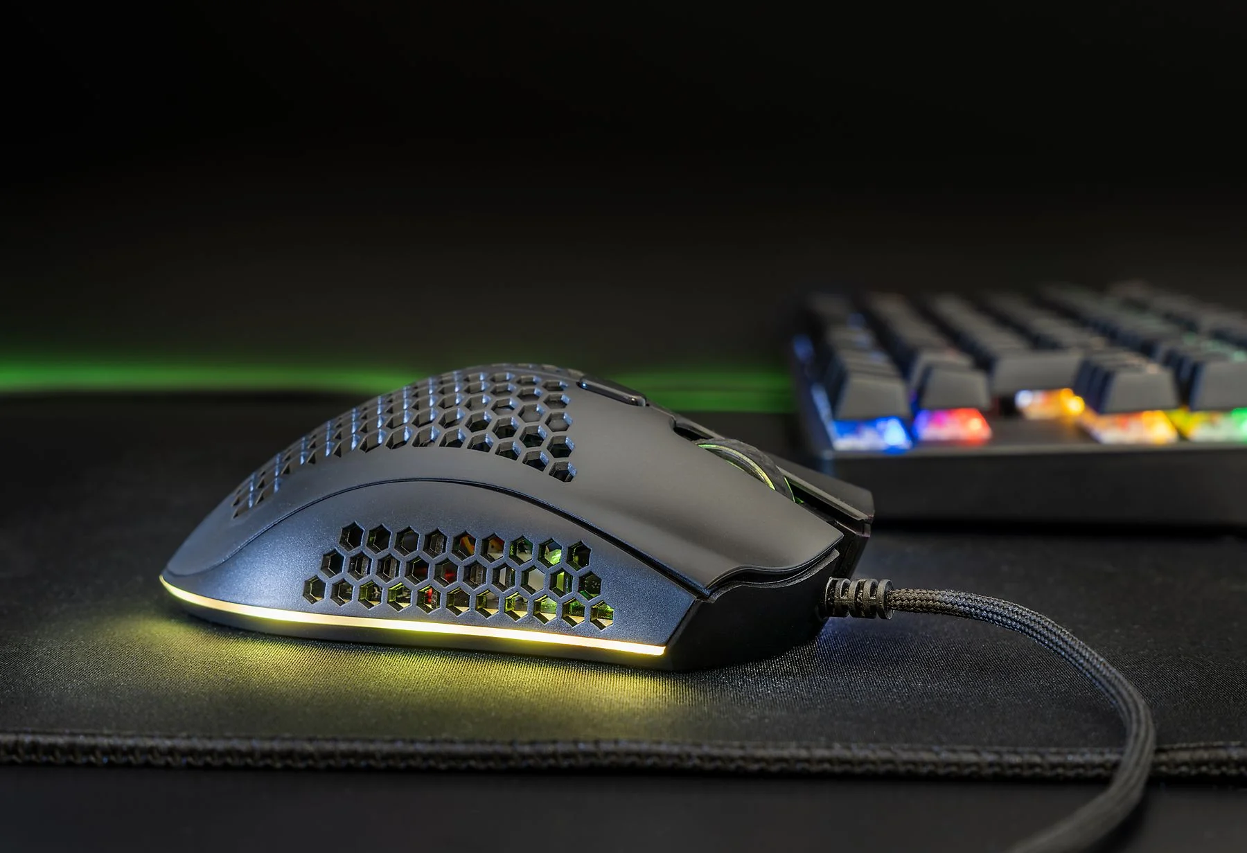 Fekete gamer egér. Méhsejtmintázat és RGB világítás. Billentyűzet a háttérben.
