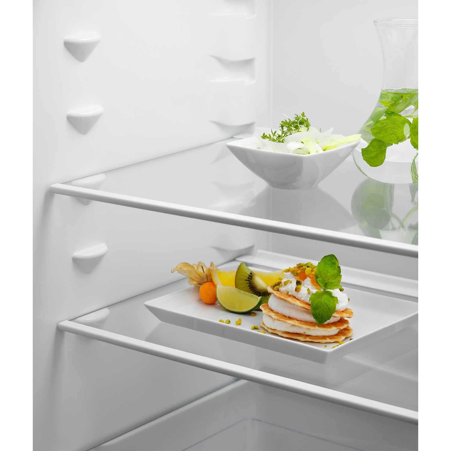 Interno frigorifero con cibo sugli scaffali. Include dessert, frutta e brocca d'acqua con menta.