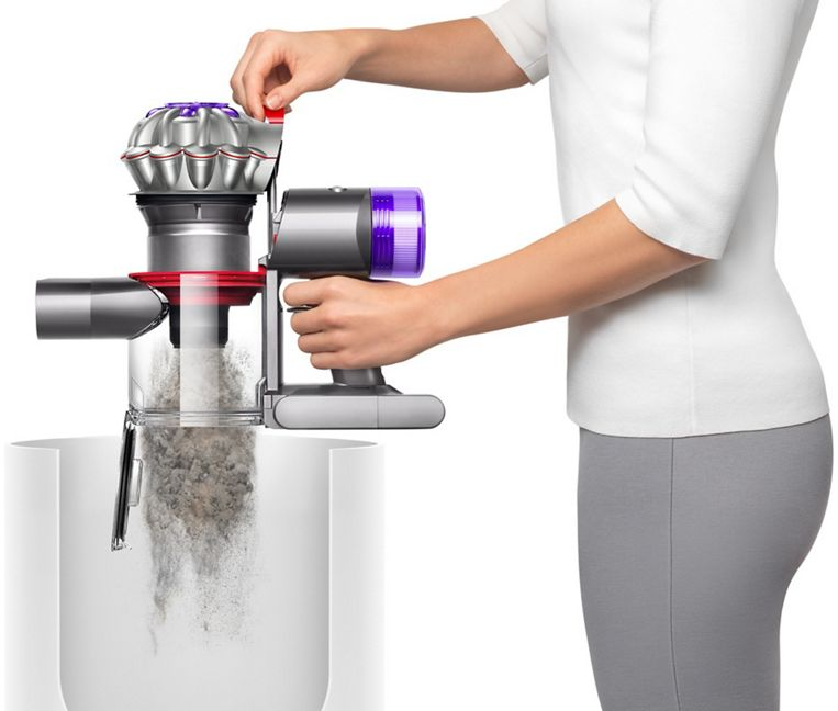 Persona che svuota un aspirapolvere Dyson grigio e viola in un contenitore trasparente.