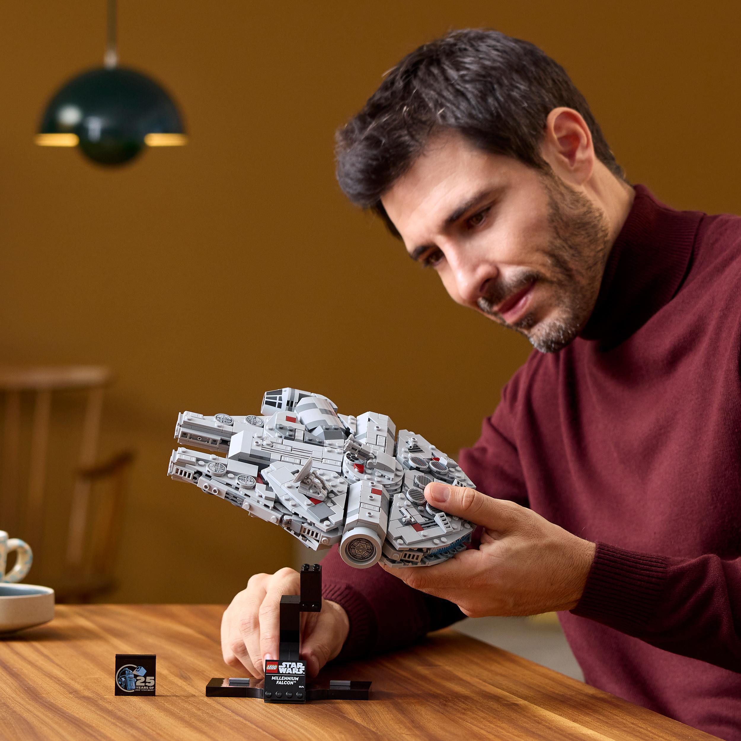 Ein Mann hält ein Star Wars Lego Set. Ein Modellraumschiff auf einem Ständer und ein kleines Etikett sind vorhanden.