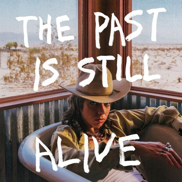 Egy nő cowboykalapban, egy fürdőkádban, a falon szöveg: 'THE PAST IS STILL ALIVE'.