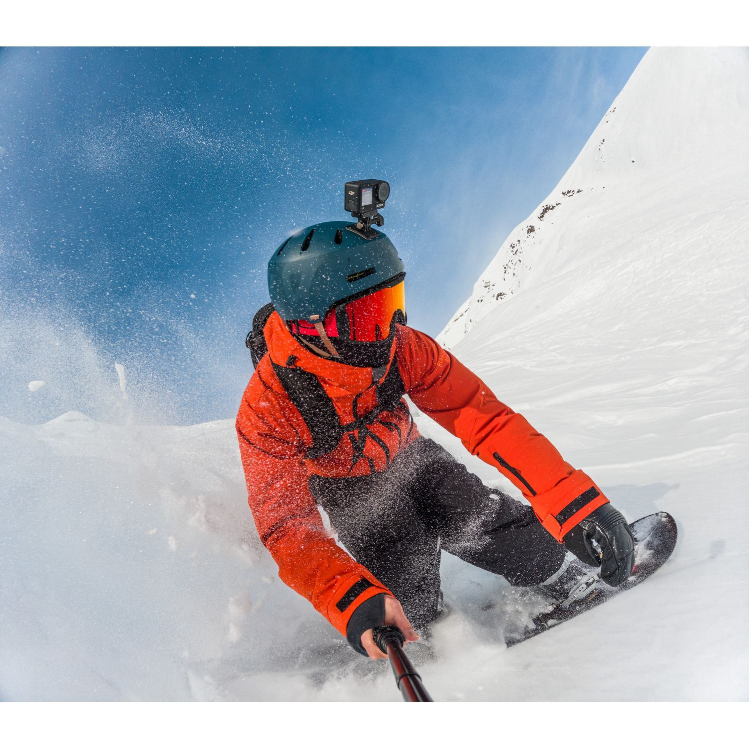 Snowboarder en veste orange sur une pente enneigée, avec une caméra GoPro sur le casque.