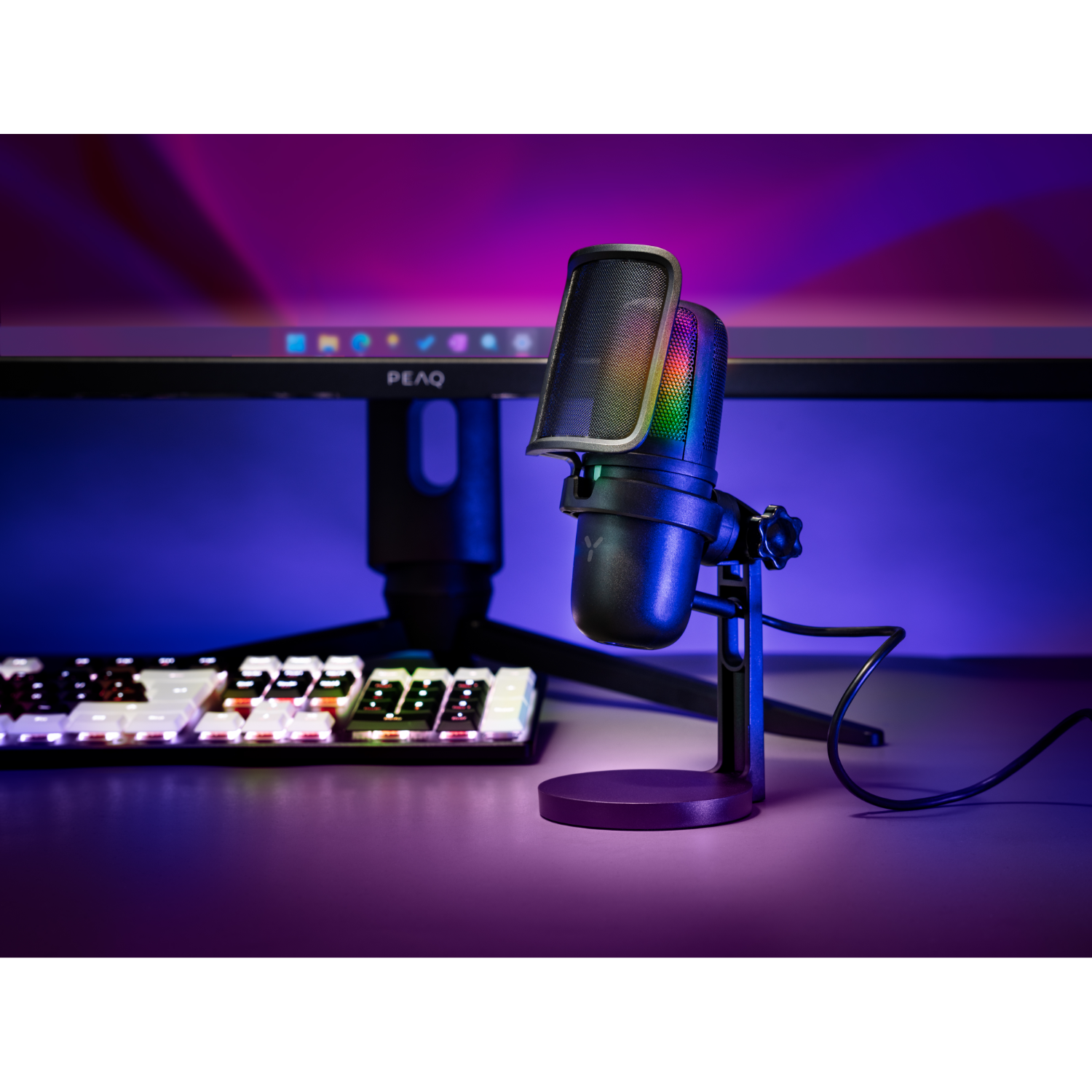 Microphone on a stand with a pop filter. Keyboard and monitor in the background.