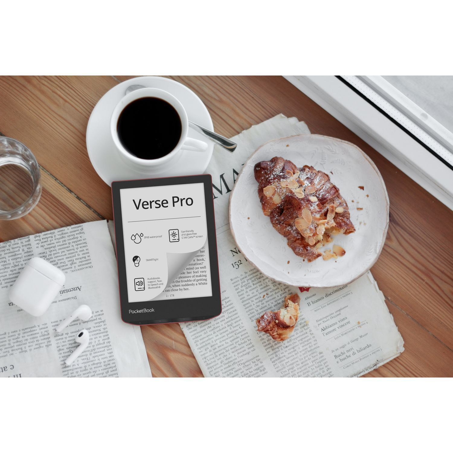 E-reader, coffee, croissant, and newspaper on a wooden table.