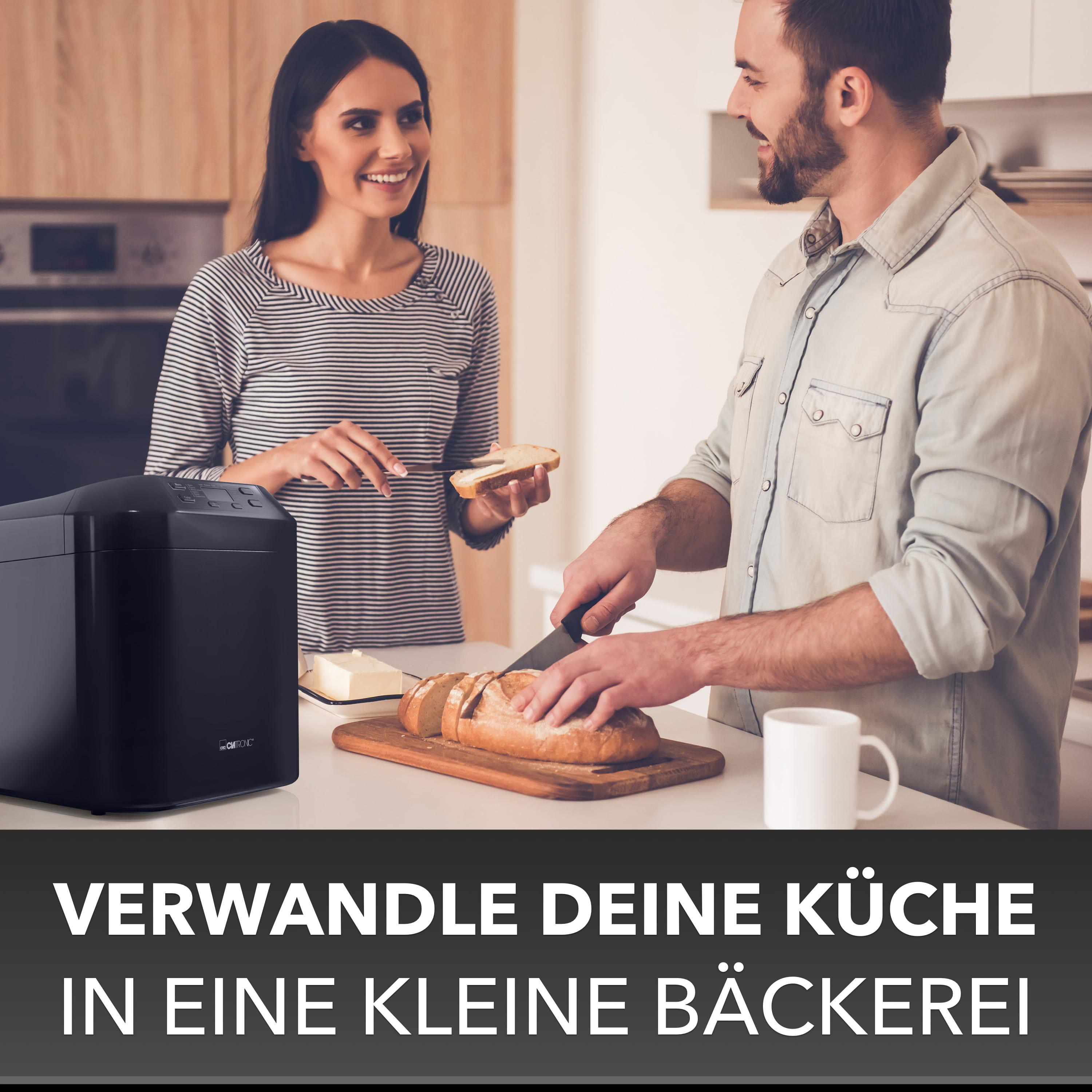 Ein Paar in einer Küche, ein Brotbackautomat und Brot auf einem Brett.