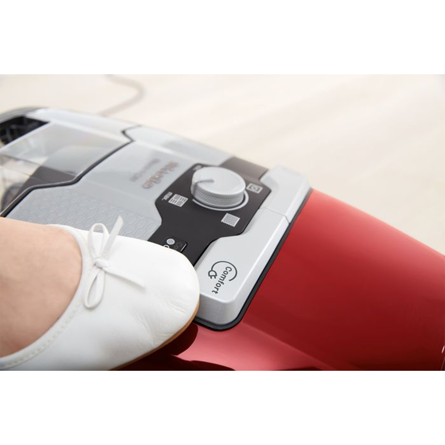 Un aspirapolvere rosso con un piede che calpesta una scarpa bianca. Logo Comfort visibile.