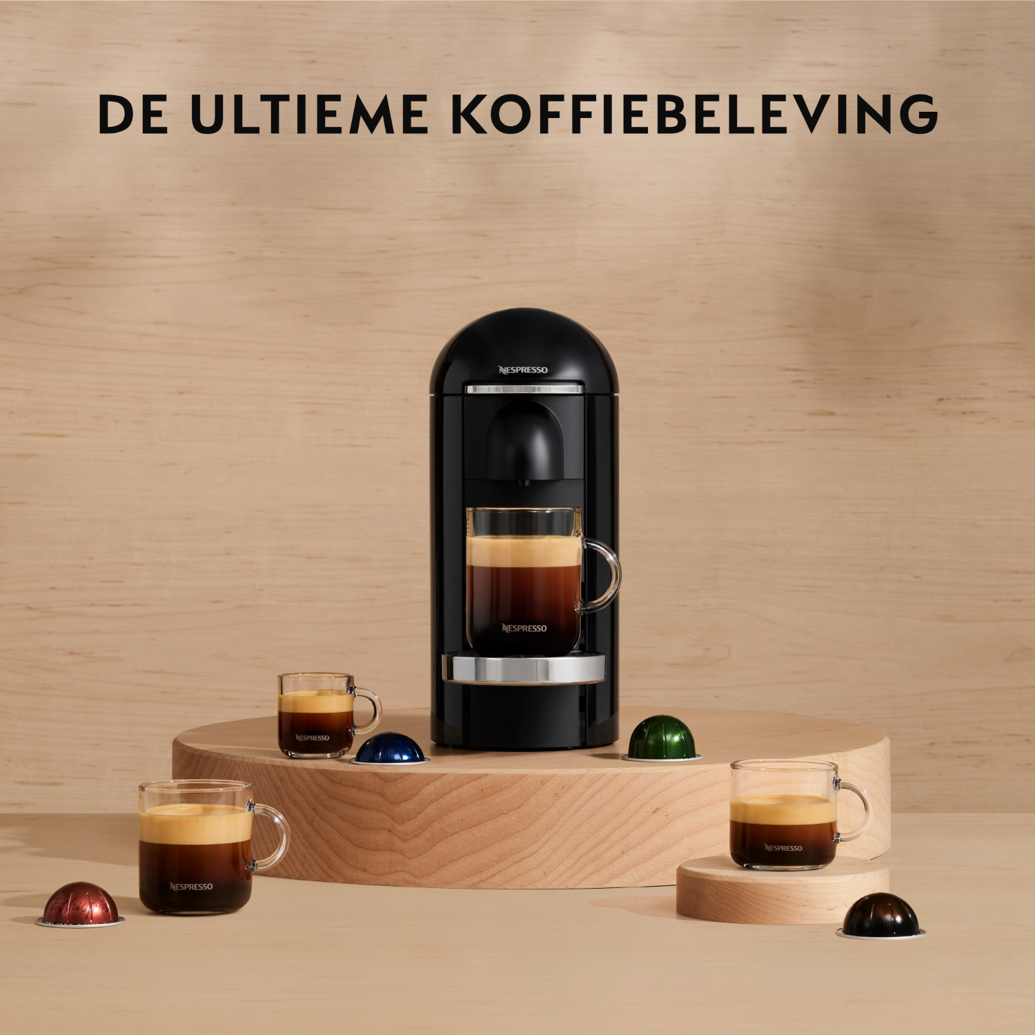 Zwarte Nespresso machine met drie koffiekopjes en capsules op een houten oppervlak.