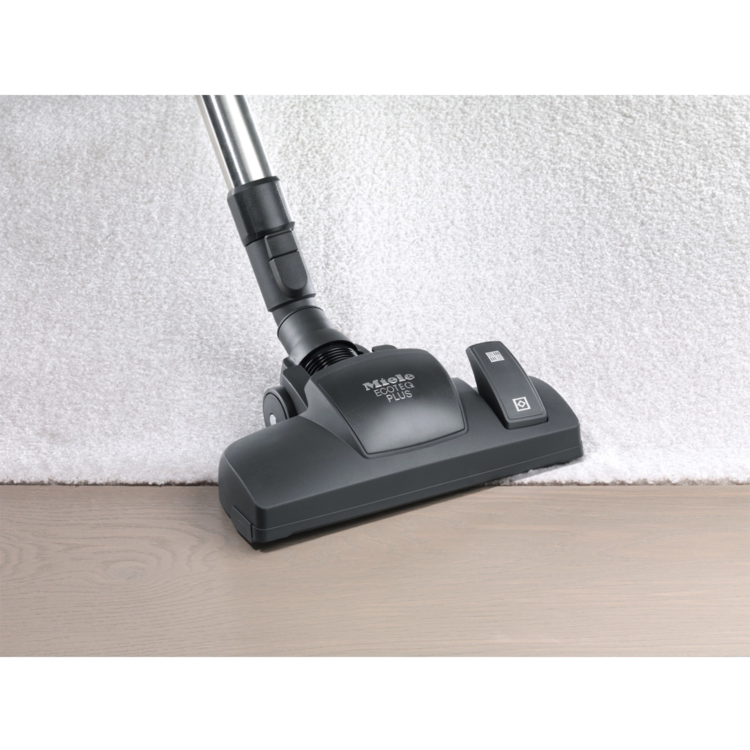 Testa dell'aspirapolvere su pavimento in legno, con tappeto bianco, testo Miele Ecoline Plus.