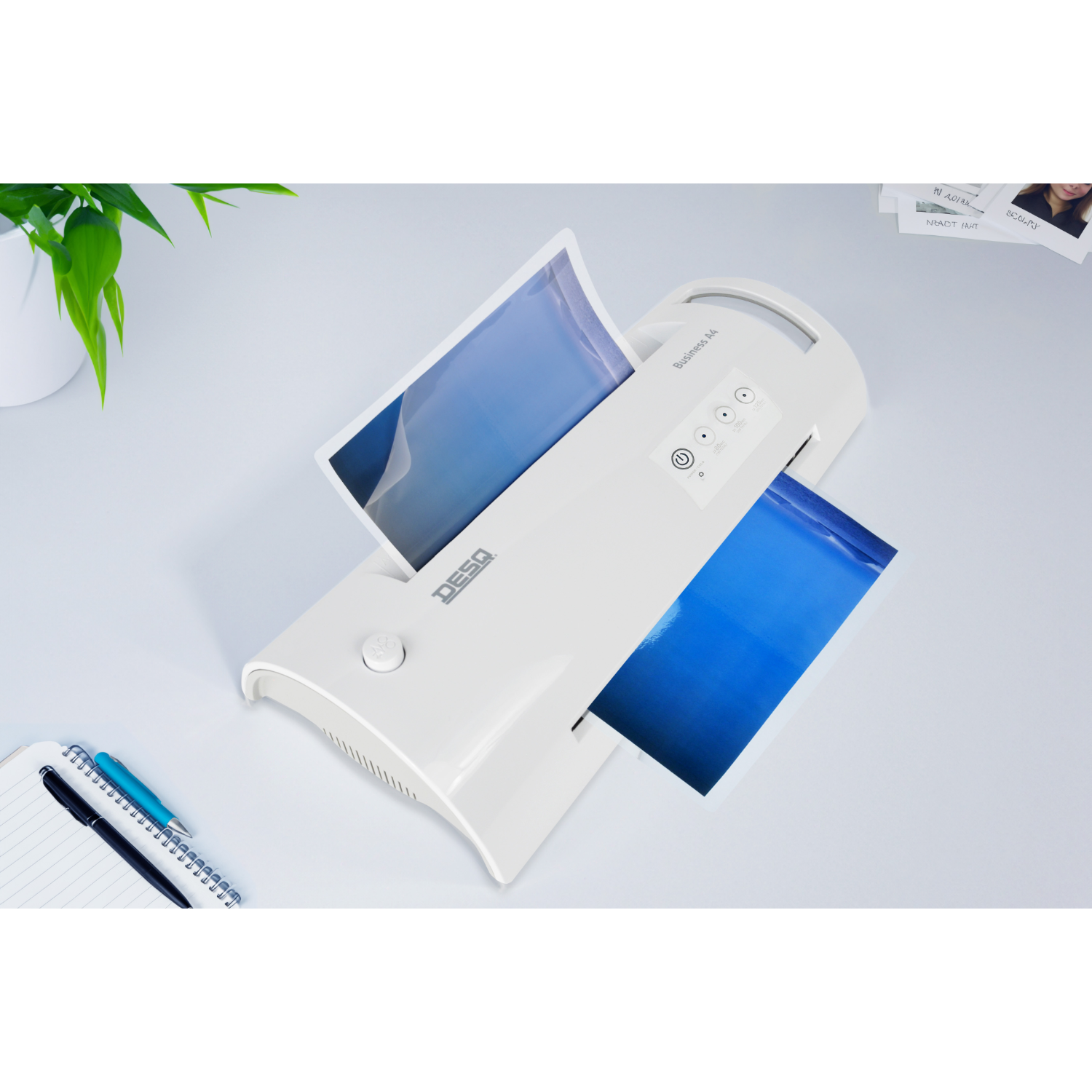White laminator with two sheets of paper inside. Blue and white background. Green plant.