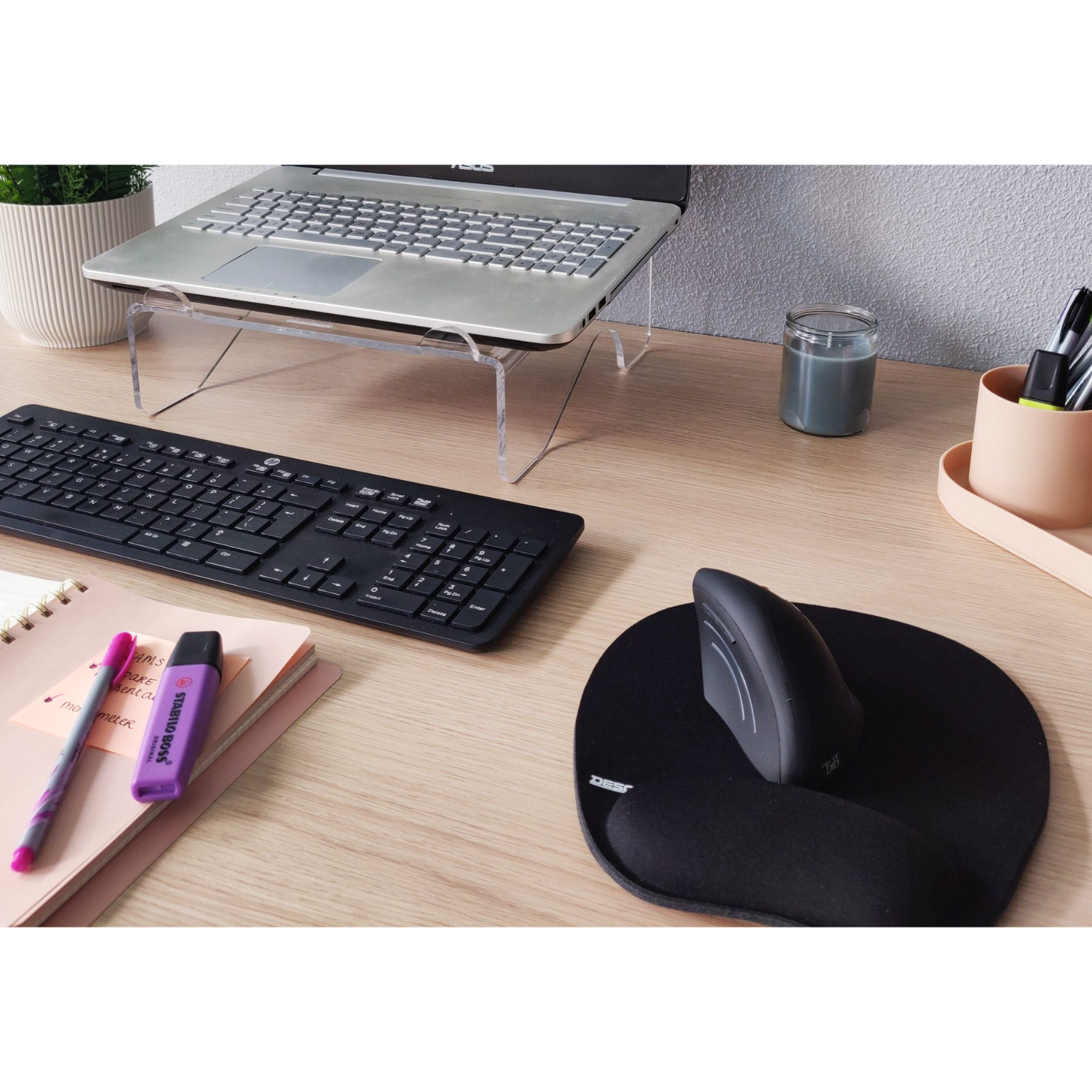 A desk with a laptop, keyboard, mouse, notebook, and a candle, all on a wood surface.