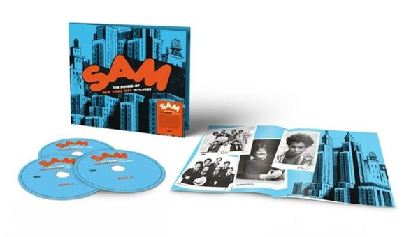 Albumcover: blaue Skyline, orangefarbenes SAM-Logo, CDs und ein offenes Booklet.