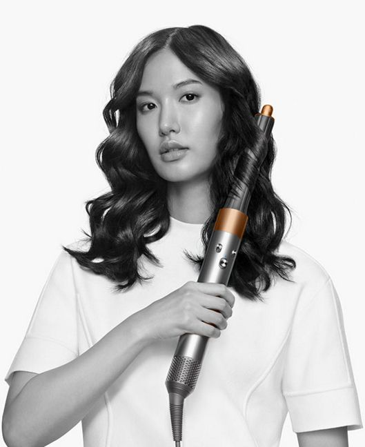 Una donna con capelli lunghi e scuri che li acconcia con un arricciacapelli Dyson Airwrap.