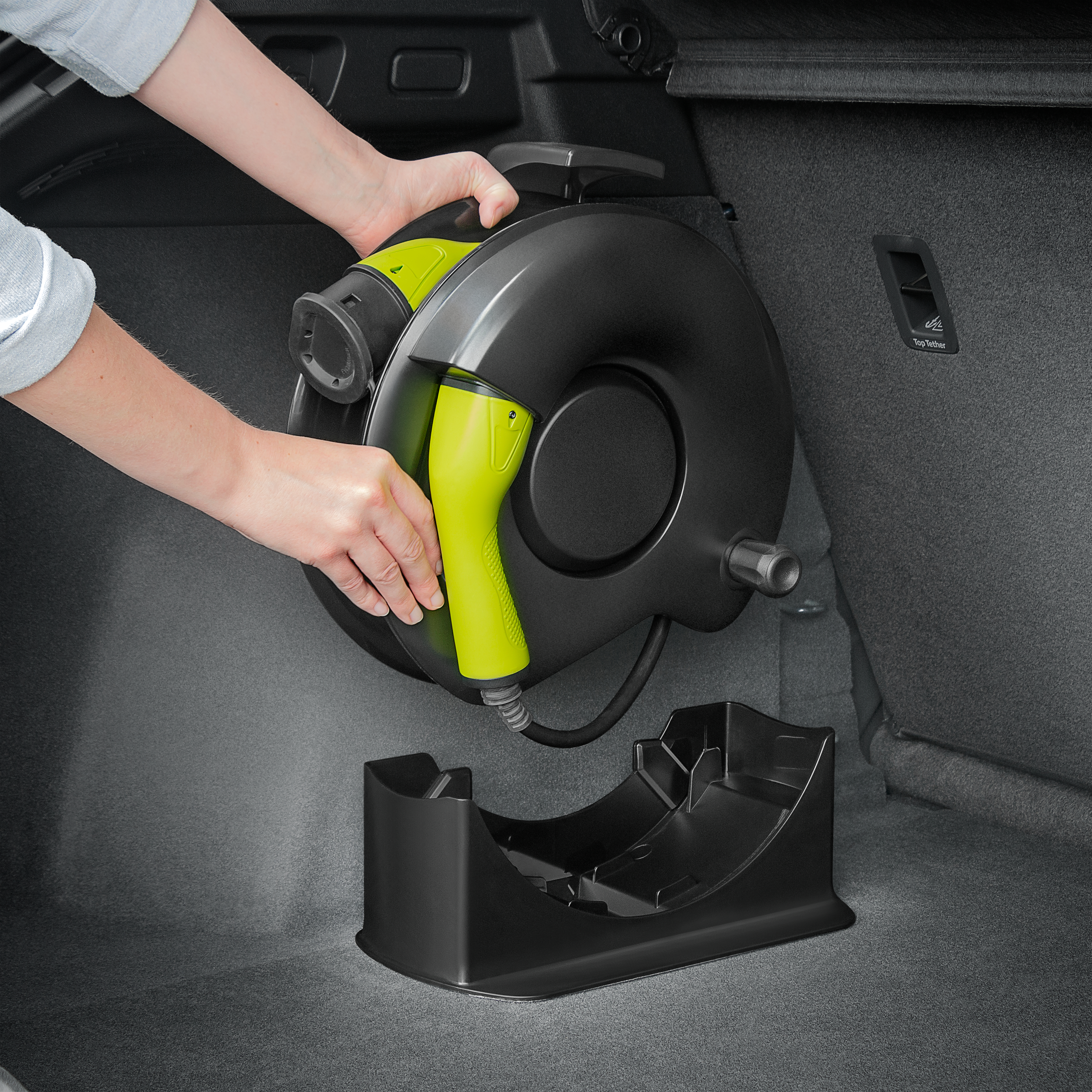 Hände handhaben eine EV-Ladekabeltrommel in einem Kofferraum.