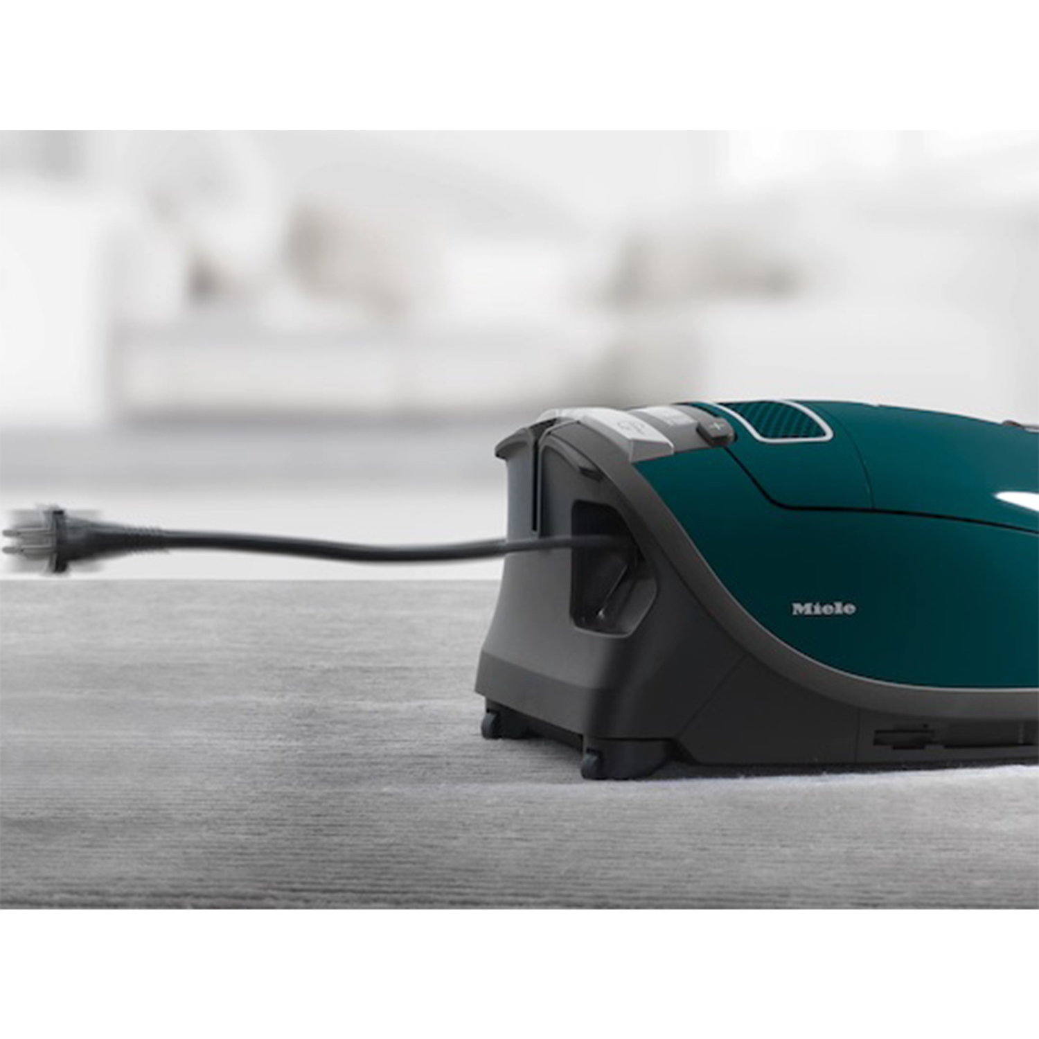 Un aspirapolvere verde scuro con il suo cavo che si estende su una superficie grigio chiaro.