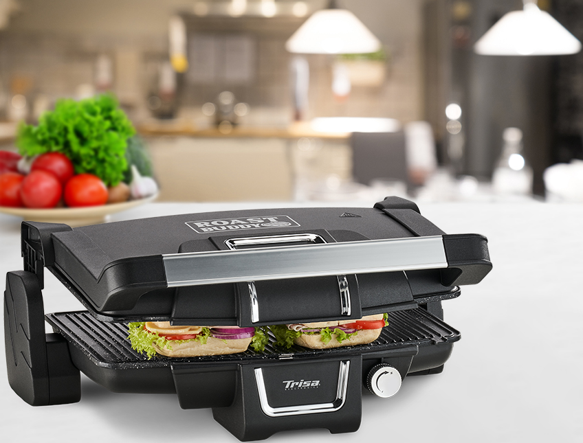 Una macchina per sandwich con due panini all'interno. Lo sfondo presenta una cucina con verdure.
