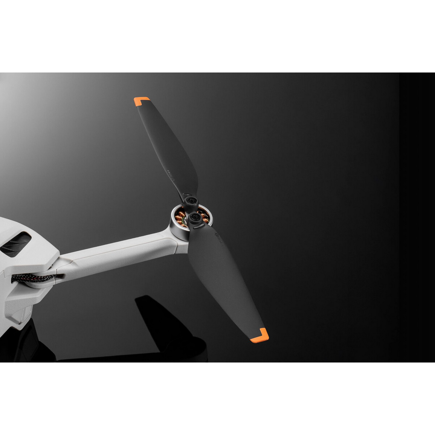 Dronepropeller met twee zwarte bladen en oranje uiteinden, tegen een zwarte achtergrond.