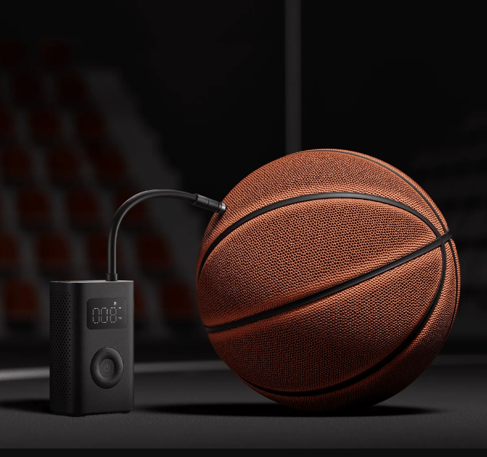 Siyah bir hava pompası ile şişirilen bir basketbol topu. Pompa ön planda, top sağda ve bulanık bir arka plan görülüyor.