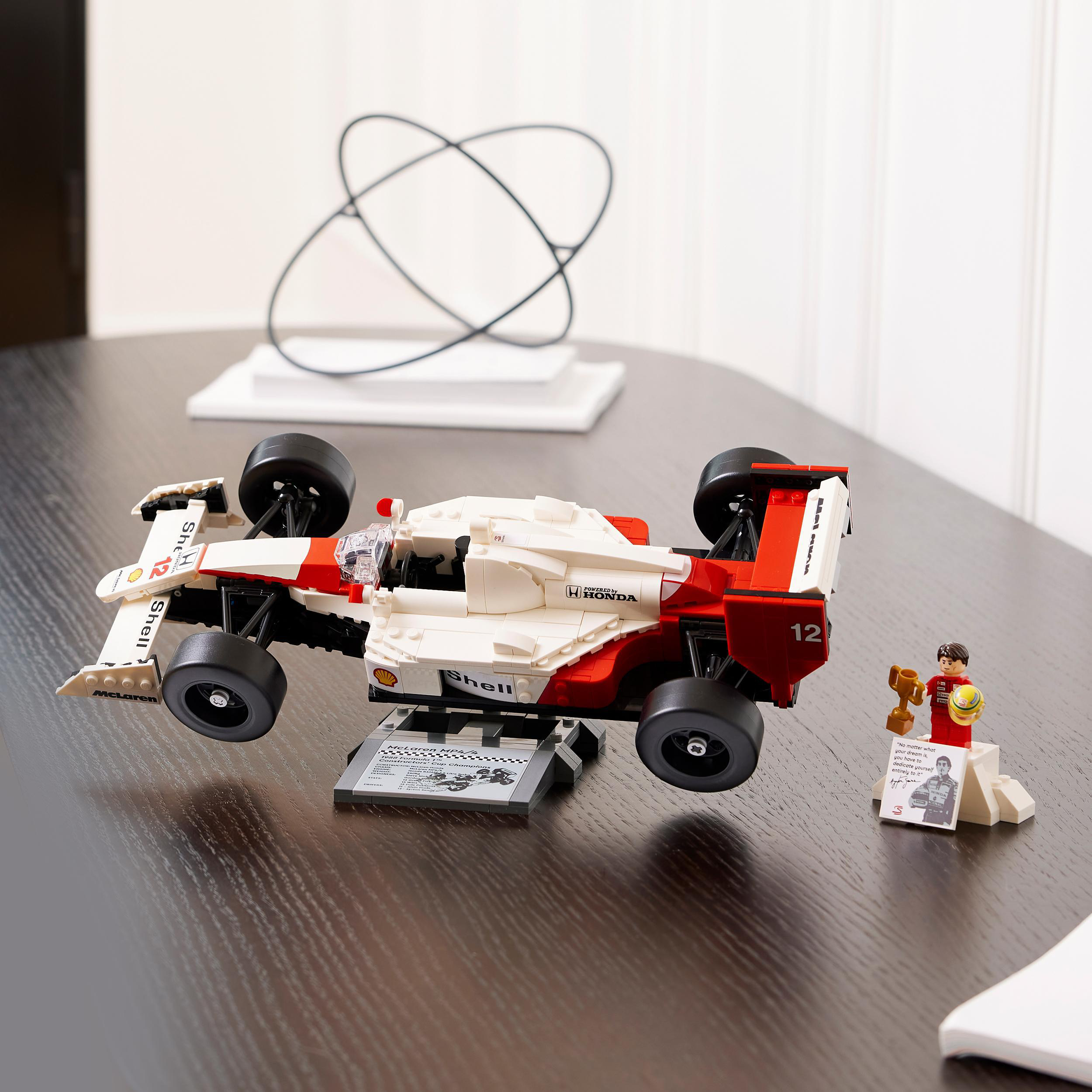 Lego-Rennwagenmodell mit Shell-, Honda-Logos, einer kleinen Figur mit Trophäe und einem Ständer.