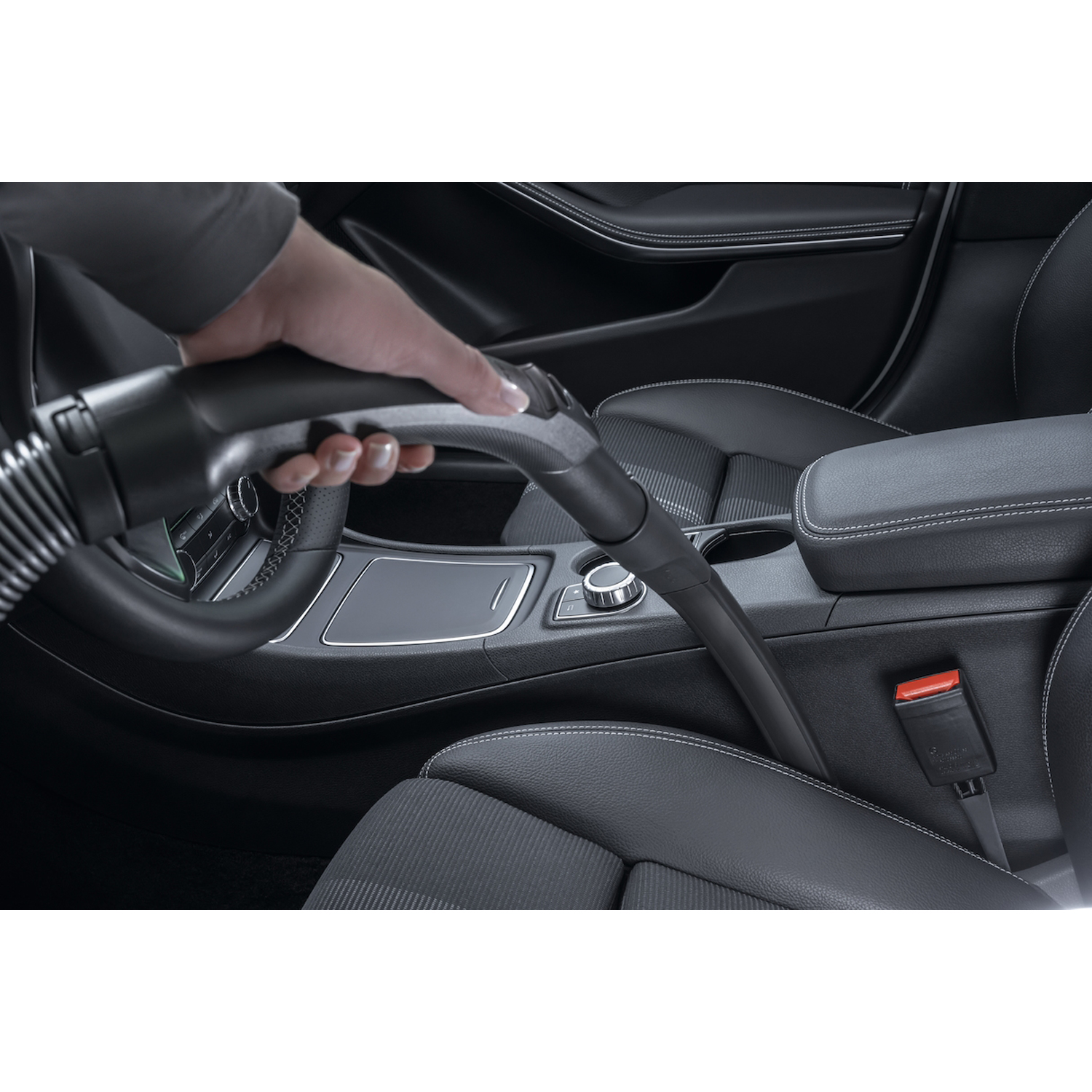 Mano che usa un aspirapolvere per pulire gli interni neri di un'auto, focalizzandosi sul sedile.