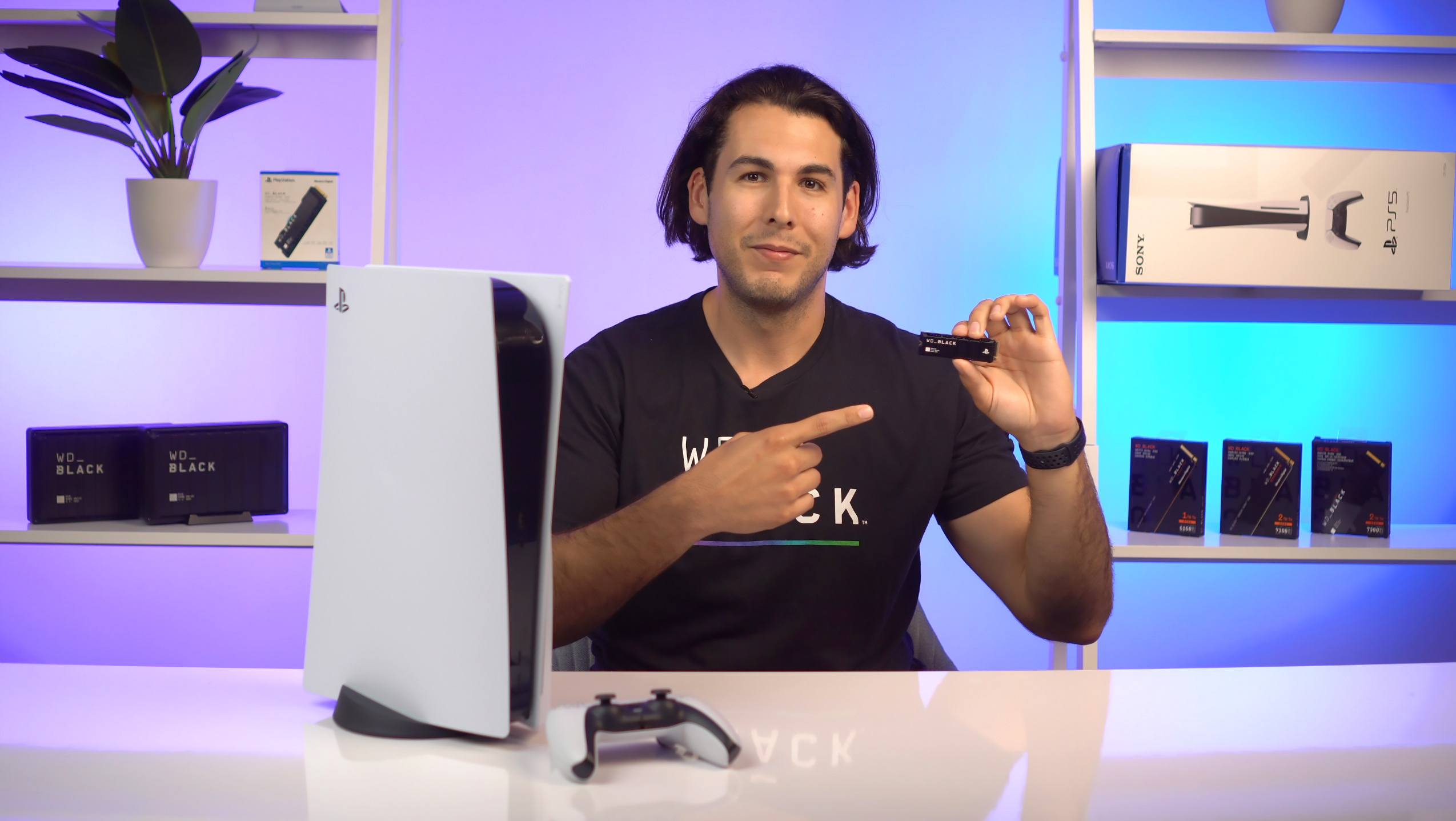 Mężczyzna trzymający WD_BLACK SSD, PS5 i inne produkty tech.