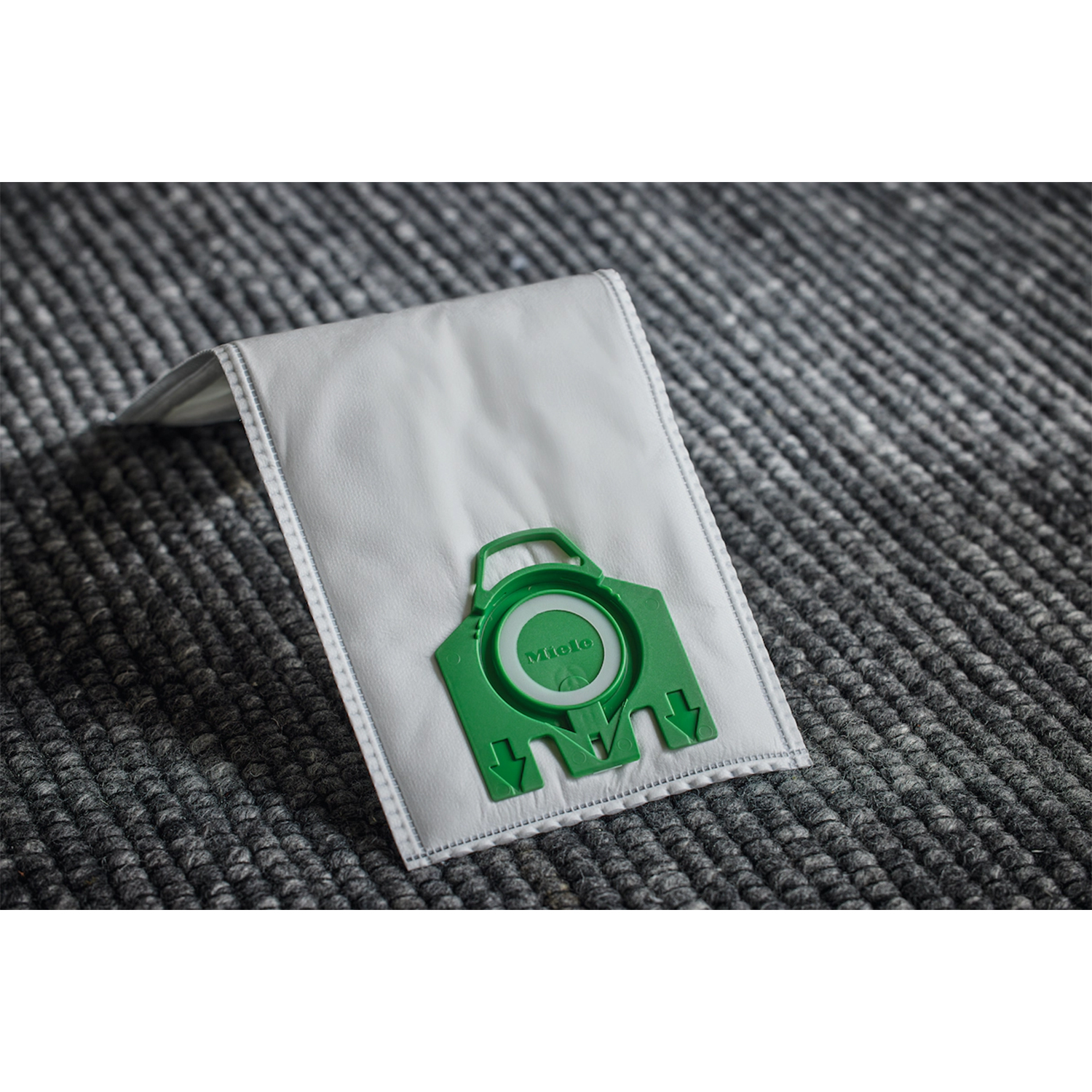 Sacchetto per aspirapolvere su moquette. Il sacchetto è bianco con un connettore verde.