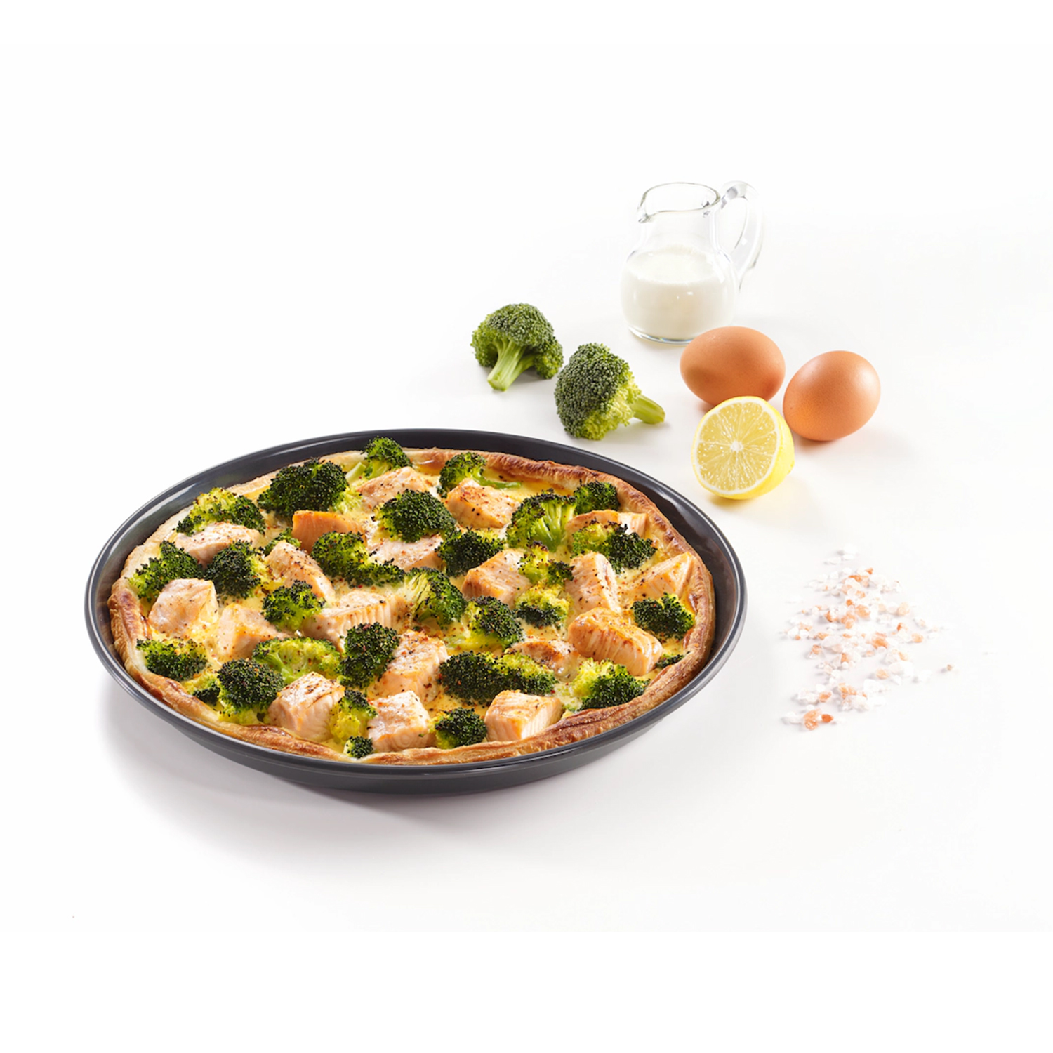 Una quiche con salmone e broccoli, uova, limone e sale su una superficie bianca.