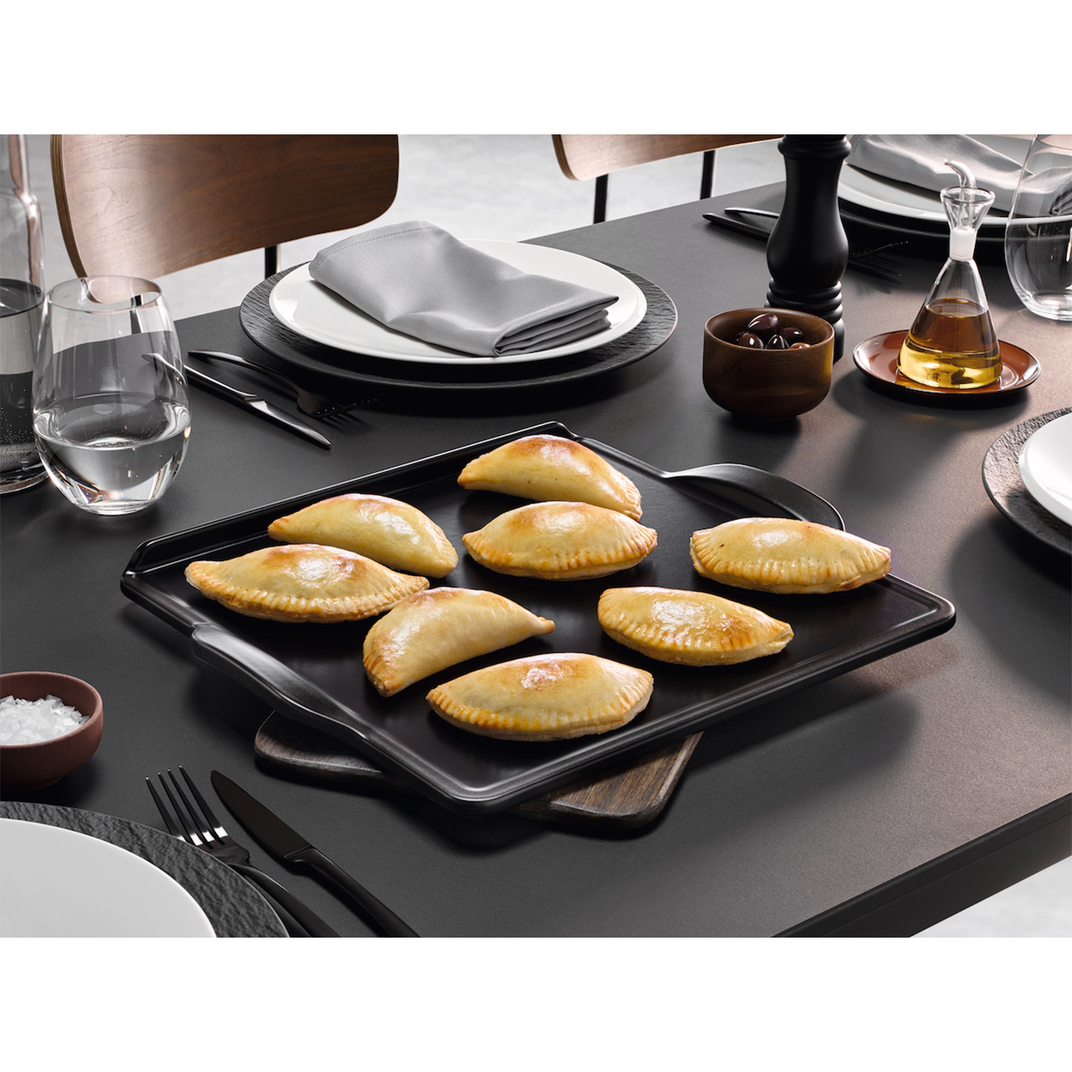 Empanadas al forno su un vassoio nero, su un tavolo con accessori per la cena.