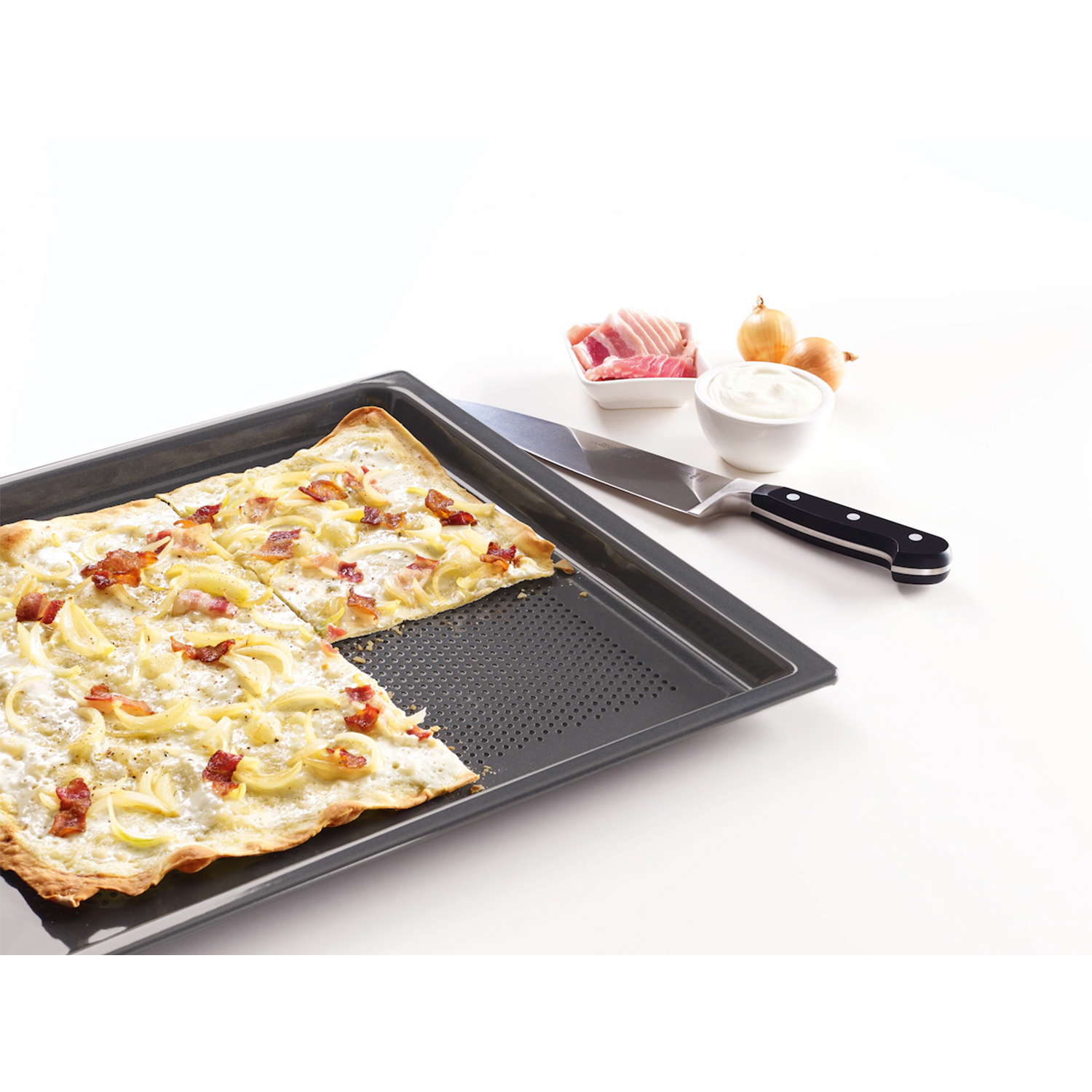 Pizza su un vassoio scuro, parzialmente tagliata, con condimenti come cipolle e pancetta, con un coltello.