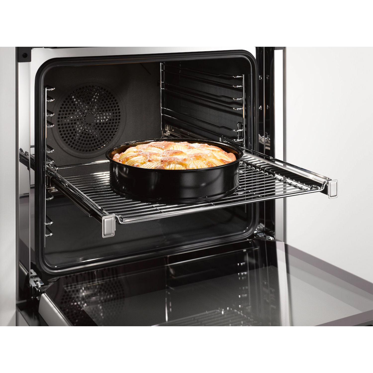 Un forno aperto con una teglia rotonda nera su una griglia estraibile, piena di torta di mele cotta.