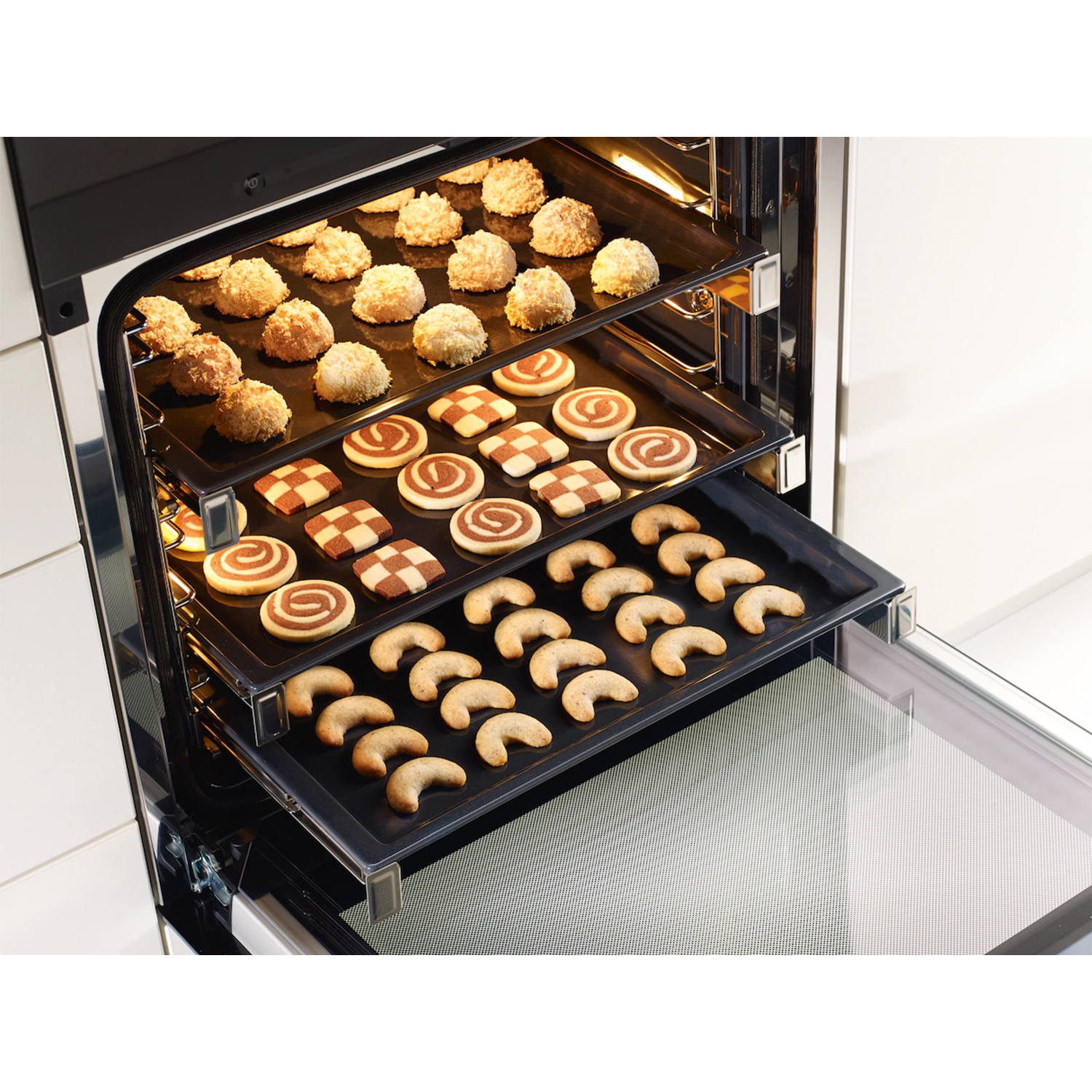 Forno con tre teglie di biscotti: cocco, scacchiera e biscotti a mezzaluna.