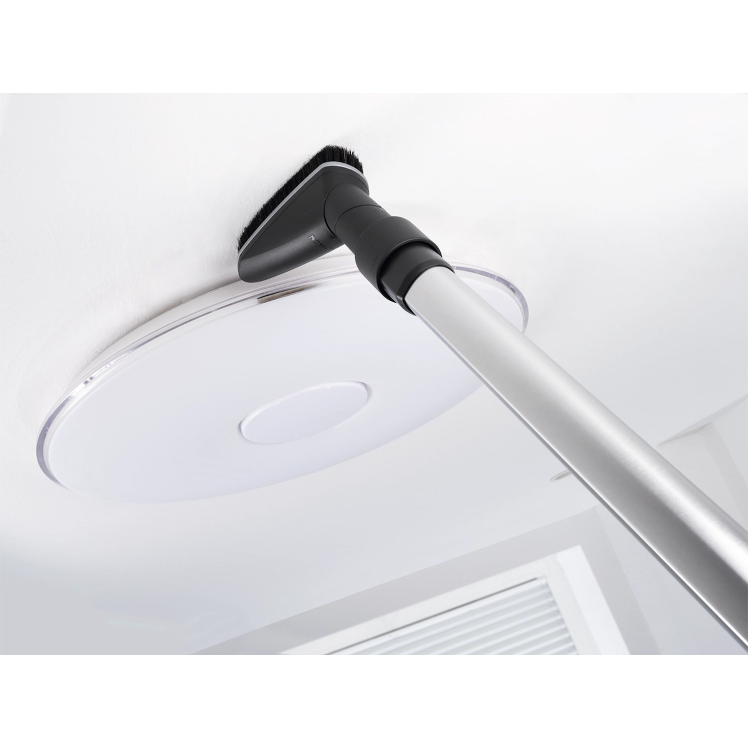 Una persona pulisce un soffitto con un accessorio per aspirapolvere. Il soffitto ha un apparecchio di illuminazione circolare.