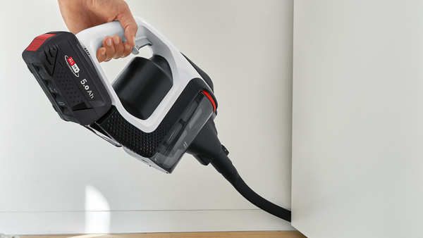 Bir el, beyaz ve siyah kablosuz bir elektrikli süpürge tutuyor. Açılı.