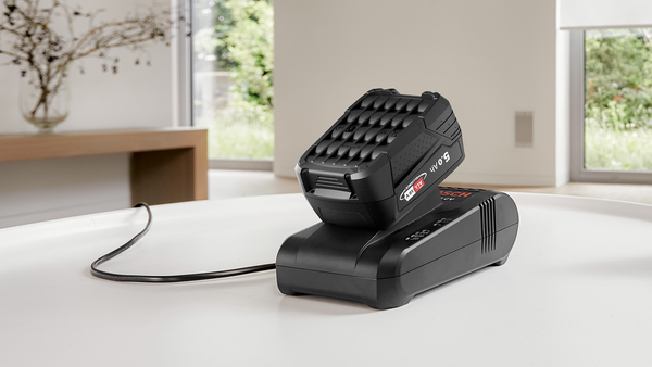 Beyaz bir masanın üzerinde, üzerinde bir pil bulunan siyah bir Bosch pil şarj cihazı.