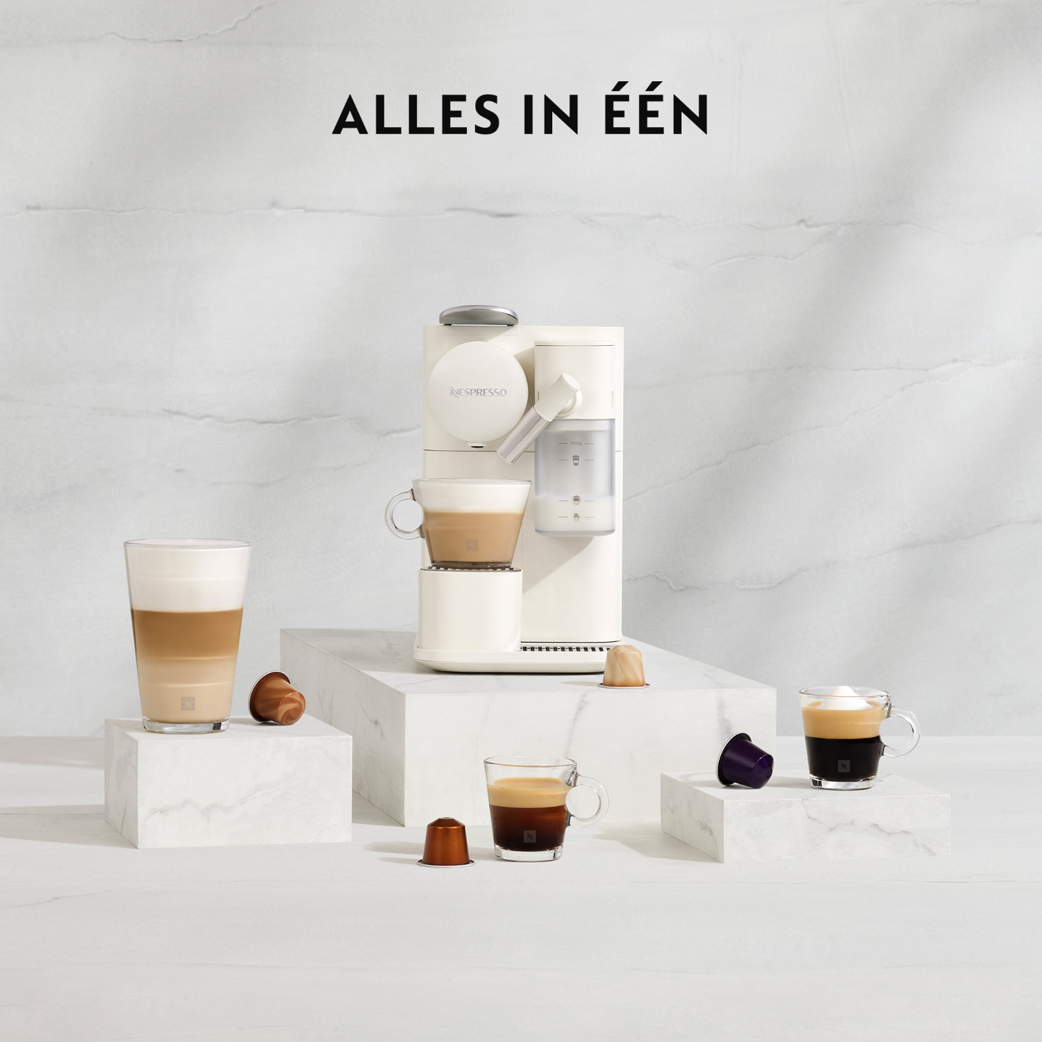 White coffee machine, cups, and coffee pods on a white surface.