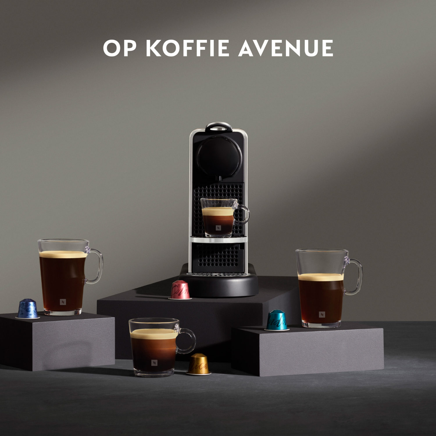 Coffee machine and cups on pedestals. Nespresso capsules next to the coffee cups.