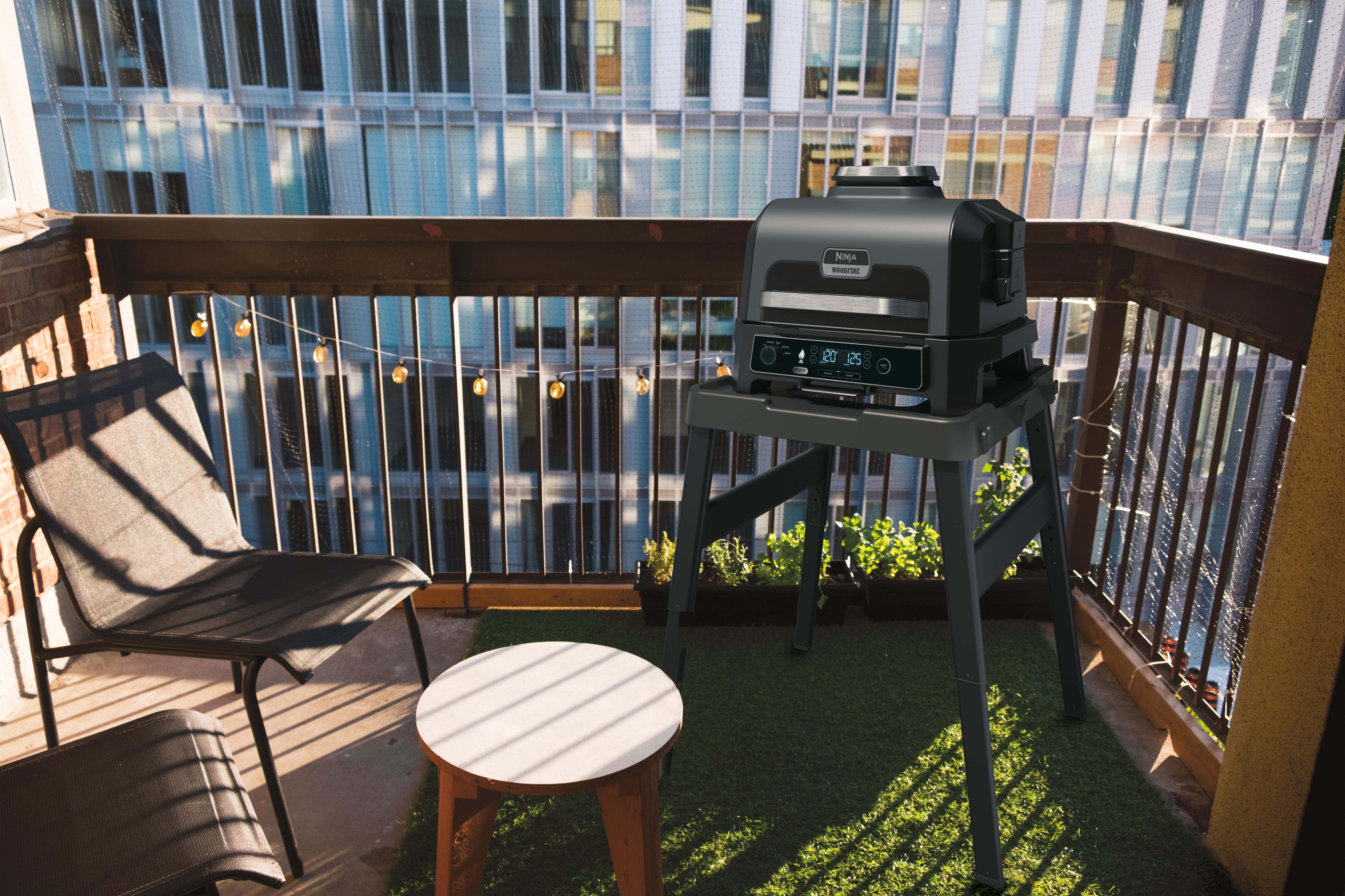 Balkon mit Grill auf einem Ständer, Tisch und Stühlen, mit Blick auf eine Stadt.