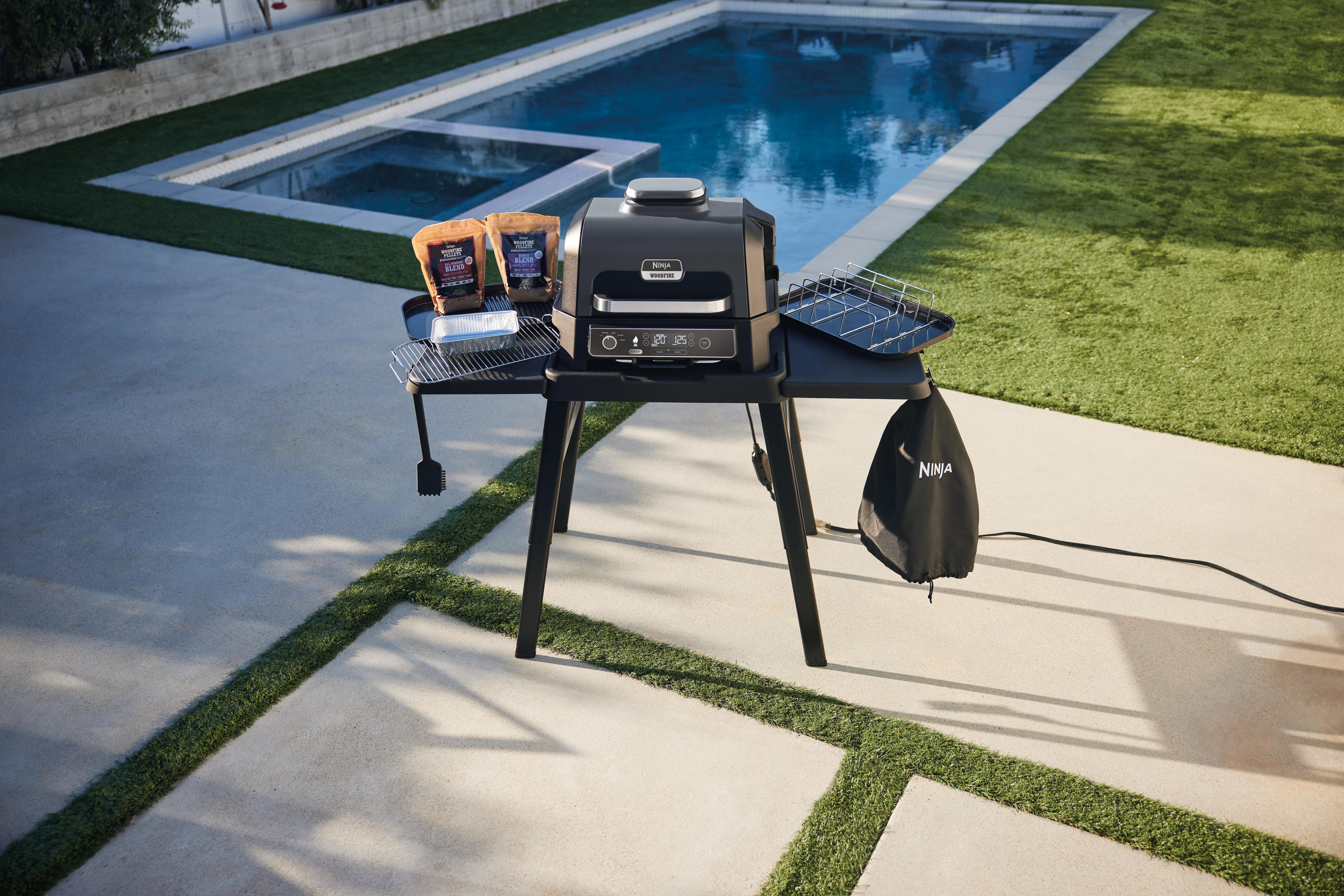 Außengrill mit Zubehör auf einem schwarzen Tisch in der Nähe eines Pools.