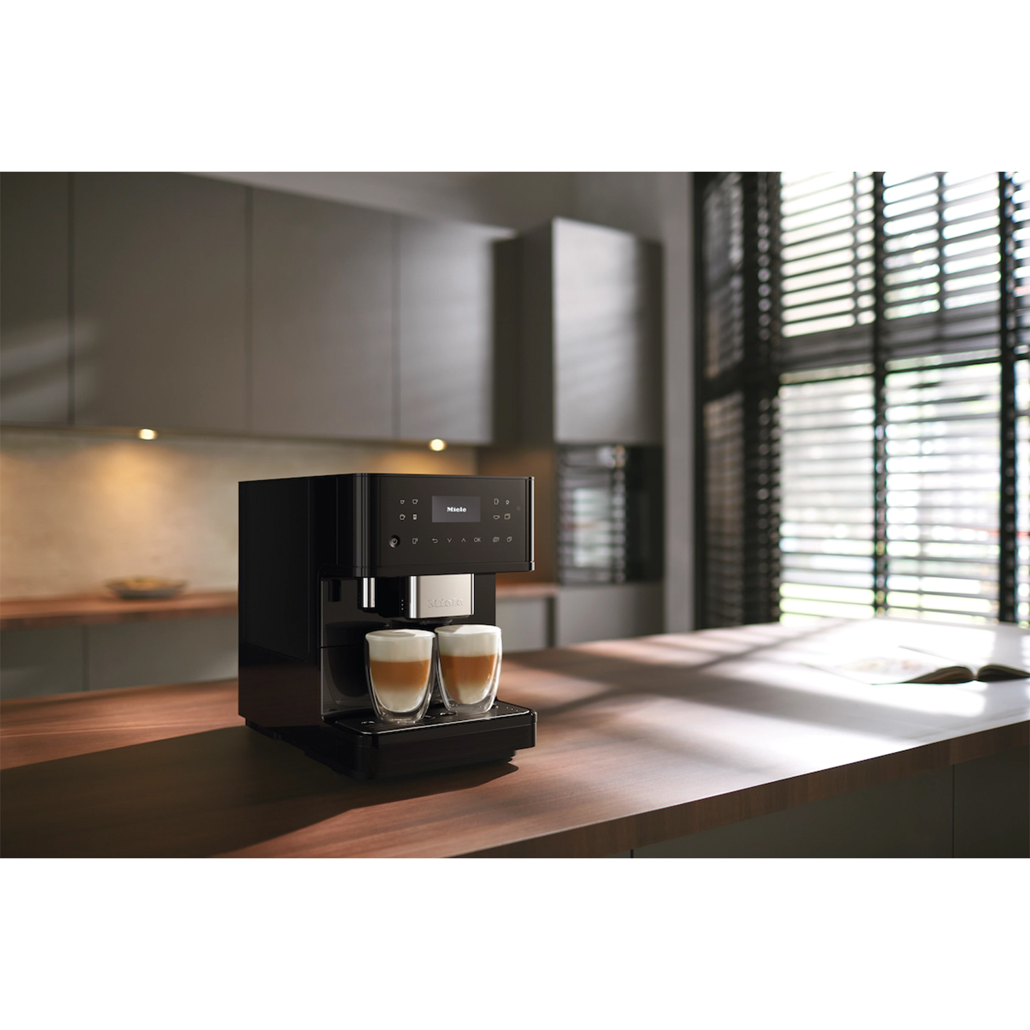 Macchina da caffè nera con due bicchieri di caffè su un piano di lavoro in legno in cucina moderna.