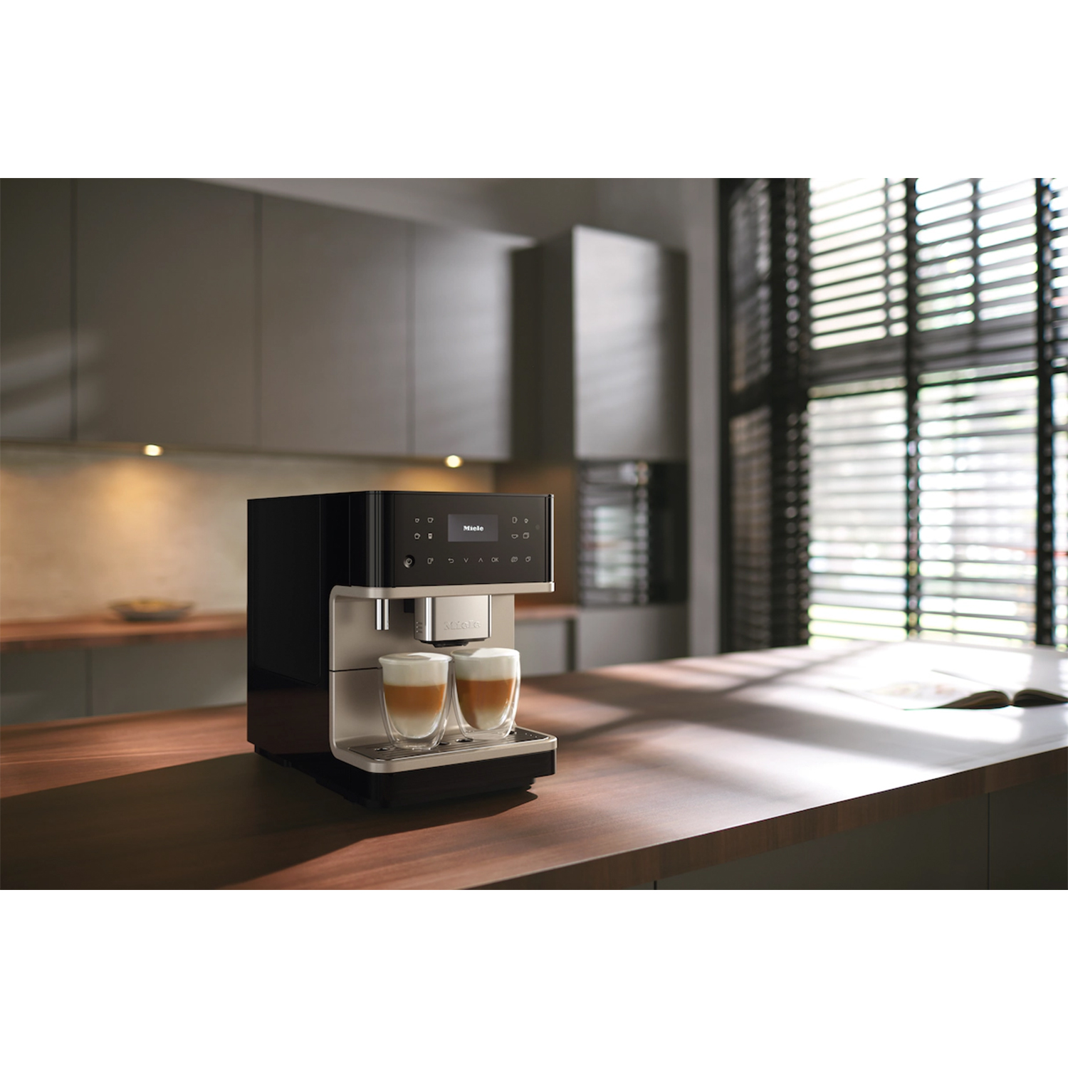 Macchina espresso che fa caffè, due bicchieri sul vassoio. Sfondo cucina.