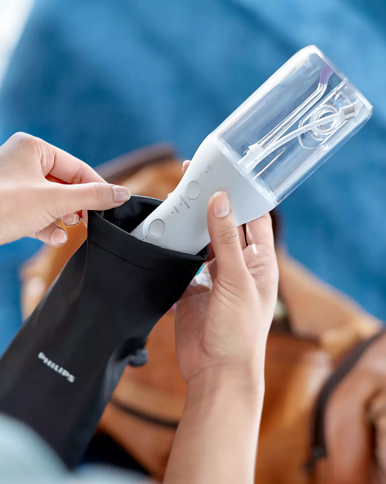 Osoba wkładająca biały irygator do jamy ustnej Philips do czarnej torby podróżnej. Rozmyte tło.