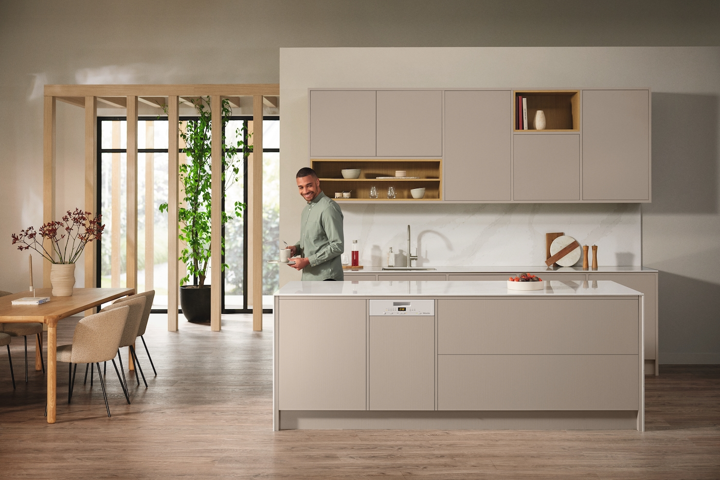 Ein Mann steht in einer modernen Küche. Die Küche ist beige mit weißen Arbeitsplatten.