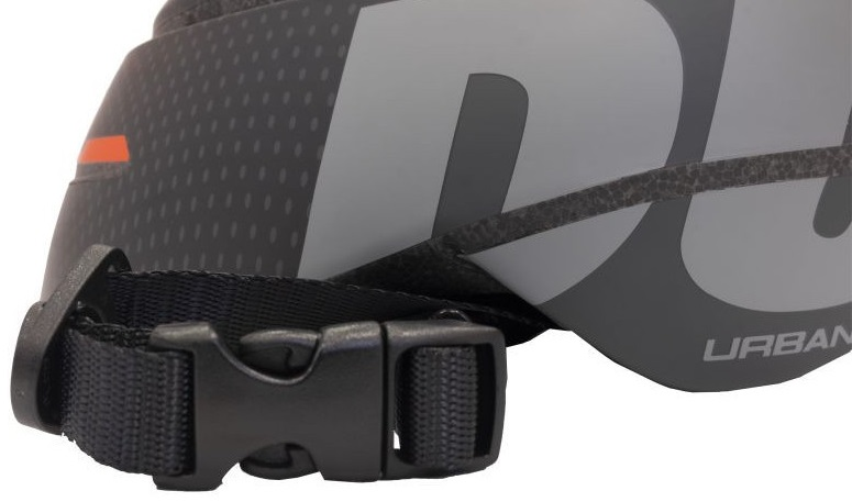 Zbliżenie paska i klamry kasku rowerowego. Czarny pasek i klamra. Słowo URBAN jest częściowo widoczne.