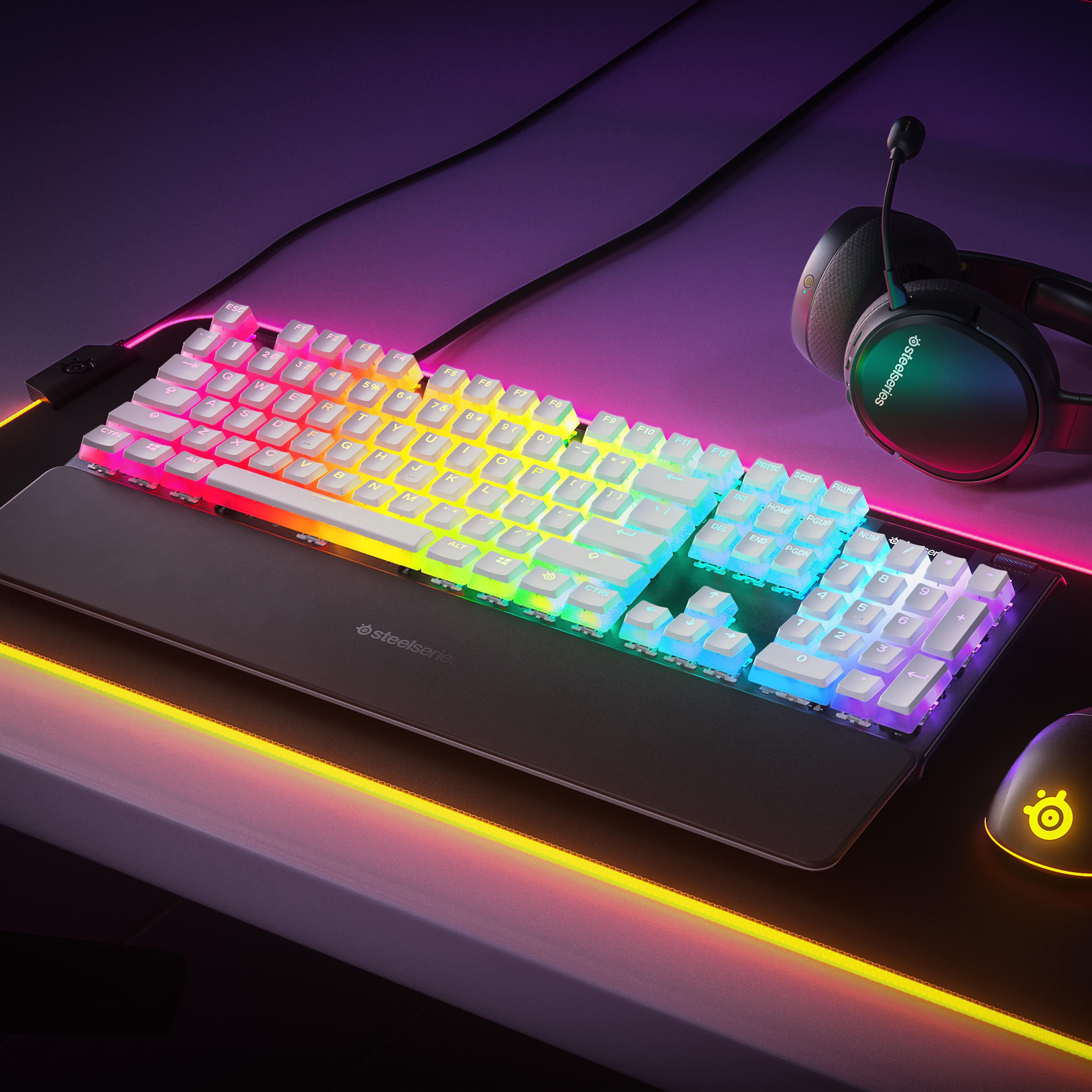 Eine Gaming-Tastatur mit Regenbogenbeleuchtung, eine Maus und ein Headset auf einem Schreibtisch.