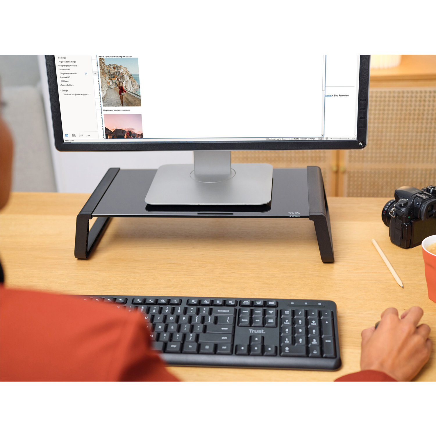 Una persona che lavora su una scrivania con un supporto per monitor, tastiera e una tazza.