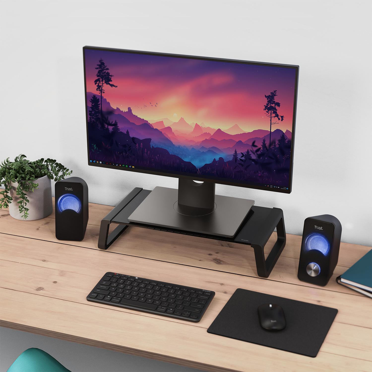 Configurazione scrivania con monitor, altoparlanti, tastiera, mouse e piccola pianta. Il monitor ha uno schermo.