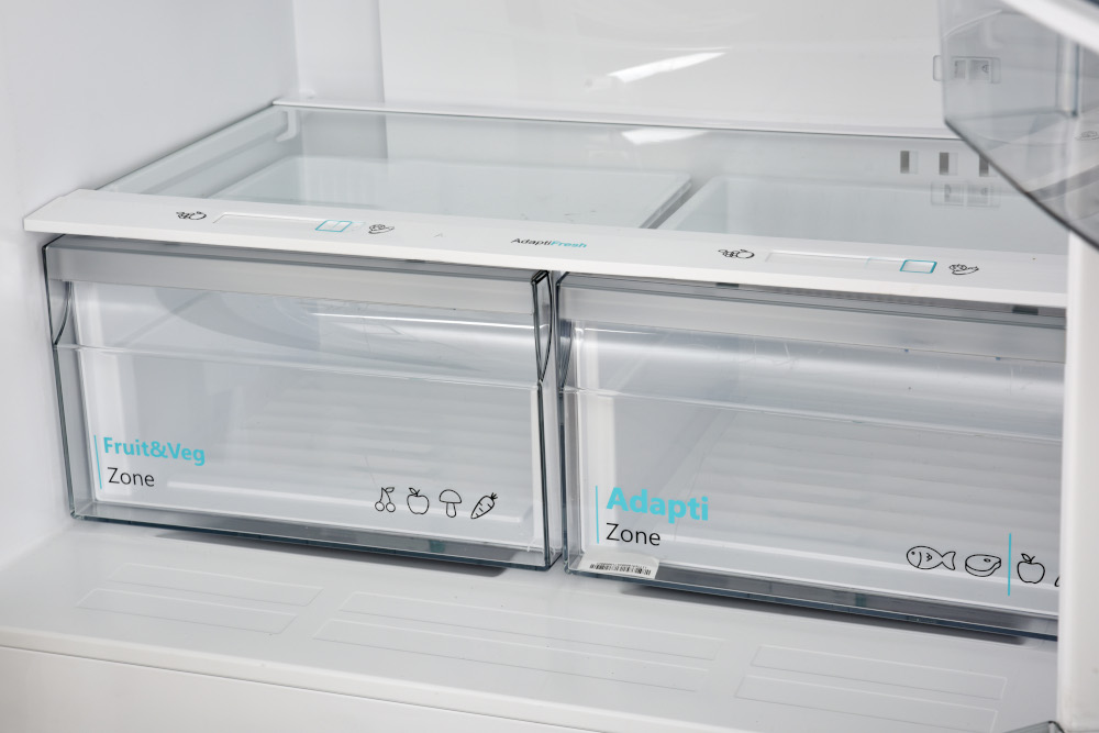 Réfrigérateur ouvert avec deux tiroirs en plastique transparent étiquetés 'Fruit & Légumes' et 'Adapti Zone'.