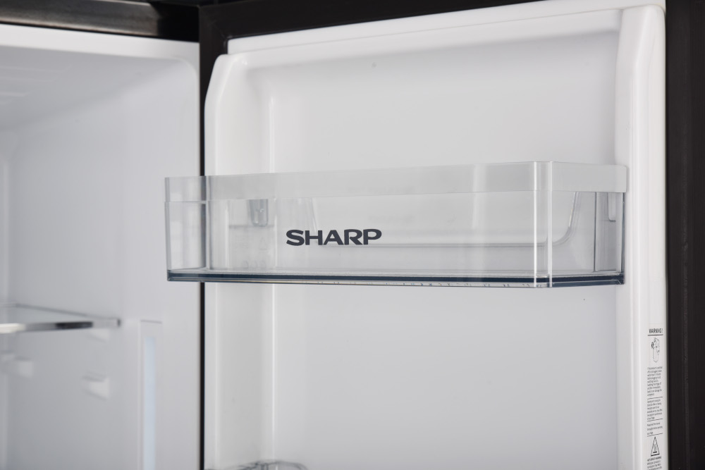 Intérieur d'un réfrigérateur avec une étagère portant l'étiquette SHARP. L'intérieur est blanc.